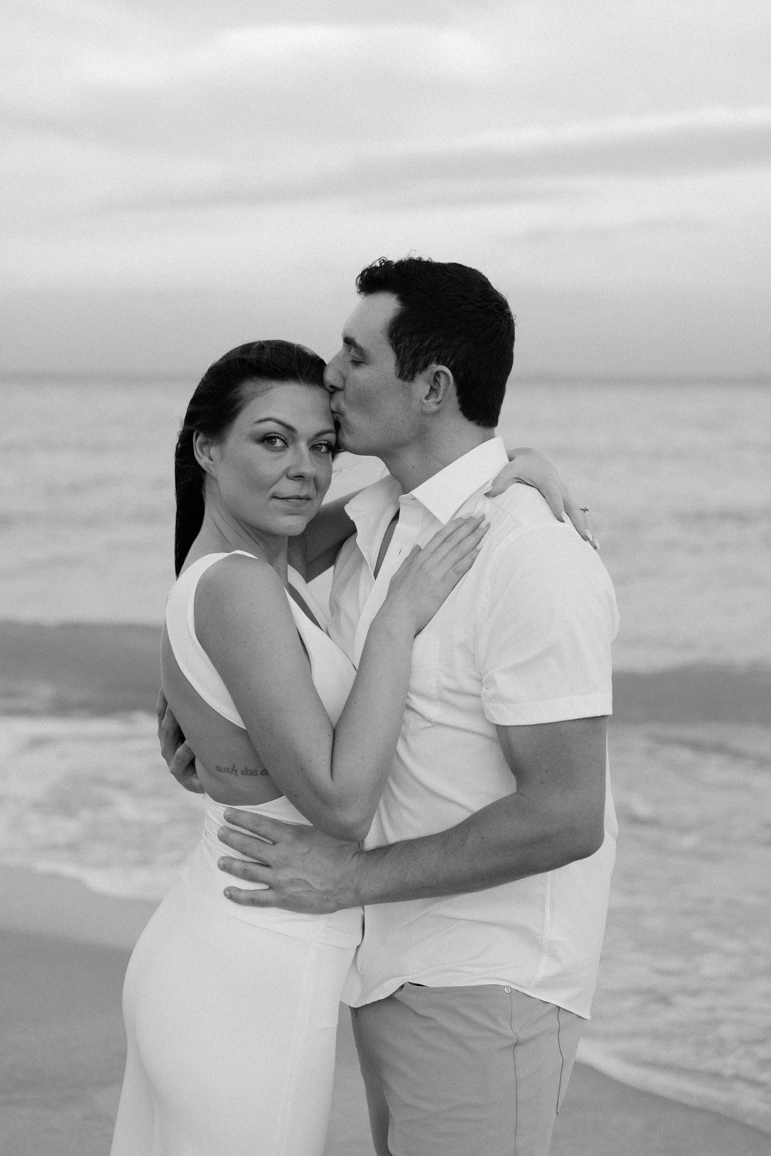 A romantic black and white photo series of a couple embracing on the beach at sunset.
