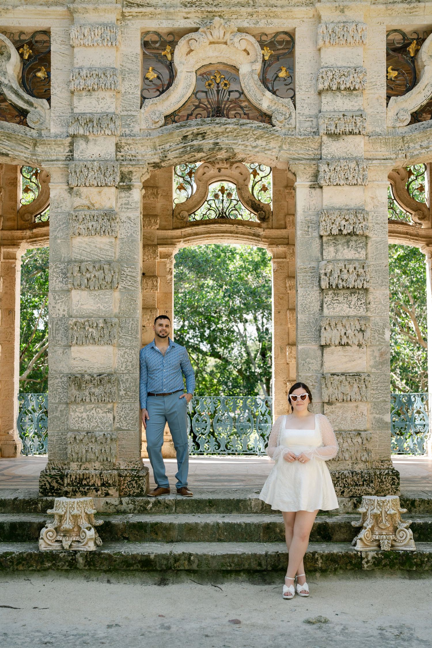 Romantic couple photoshoot in a historic stone colonnade with ornate architectural details and natural lighting.