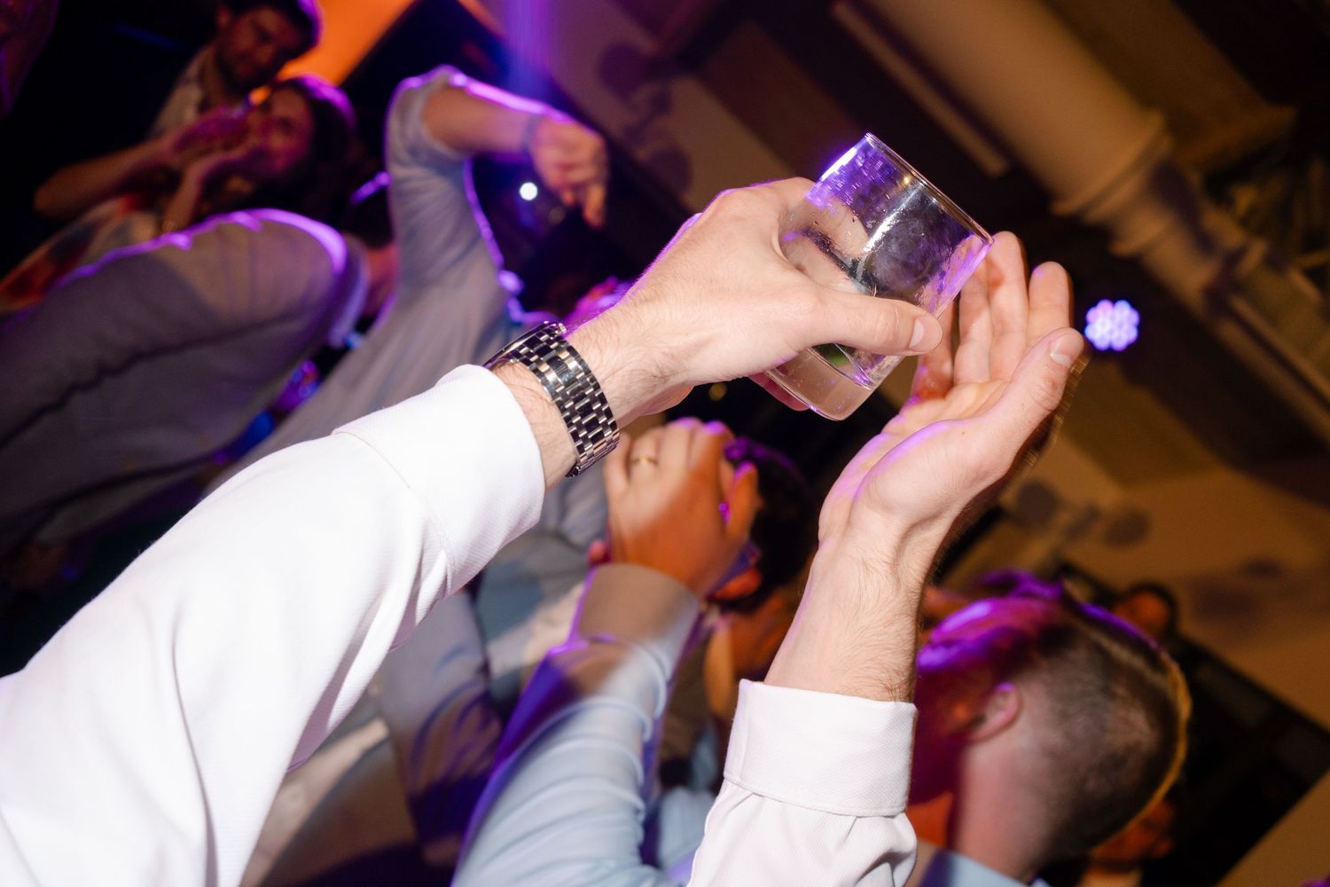 Hands pouring drinks at a party with blue lighting and a festive atmosphere.
