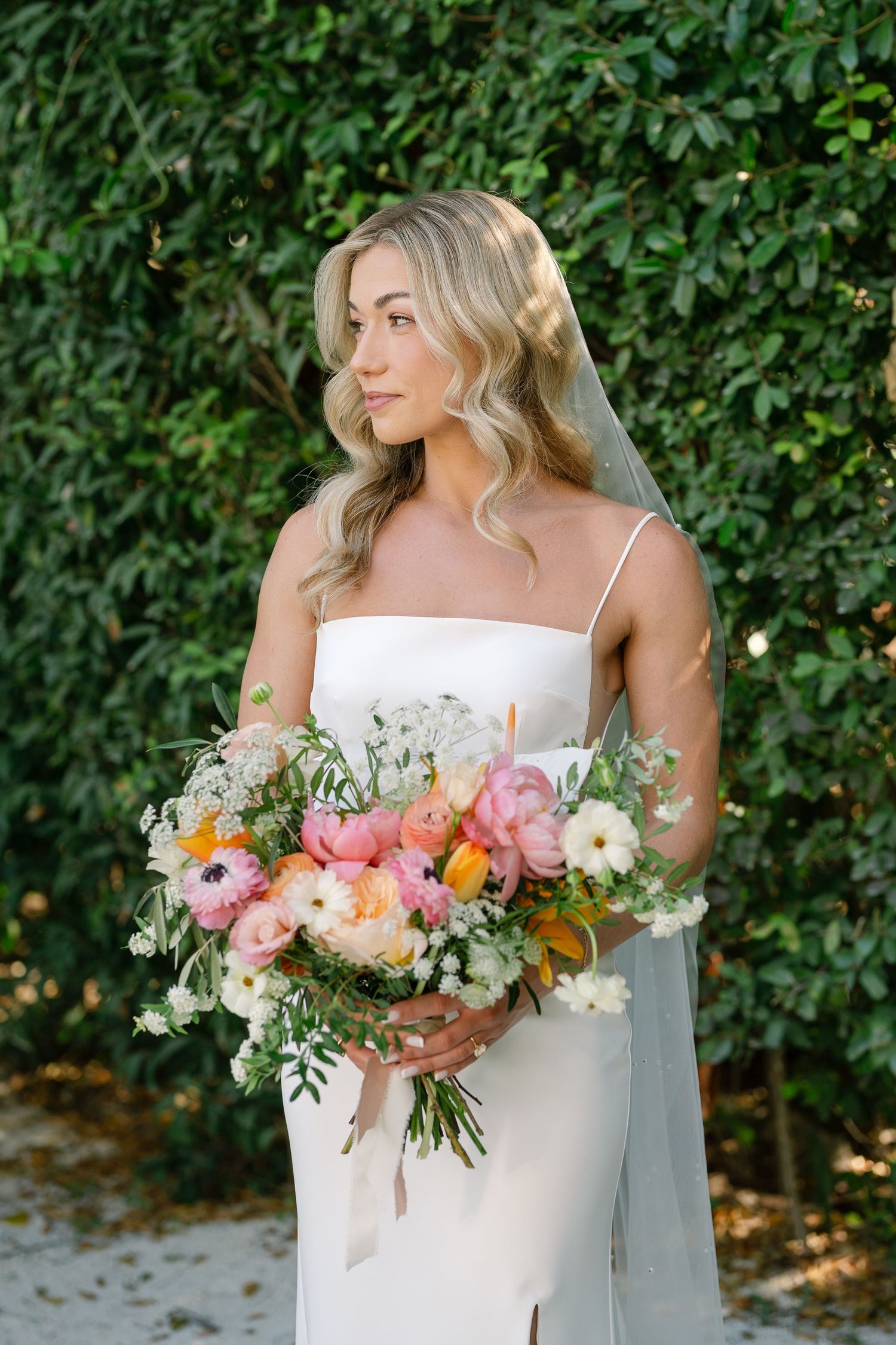 Bridal bouquet featuring pink, peach and white flowers with delicate greenery against a garden backdrop.