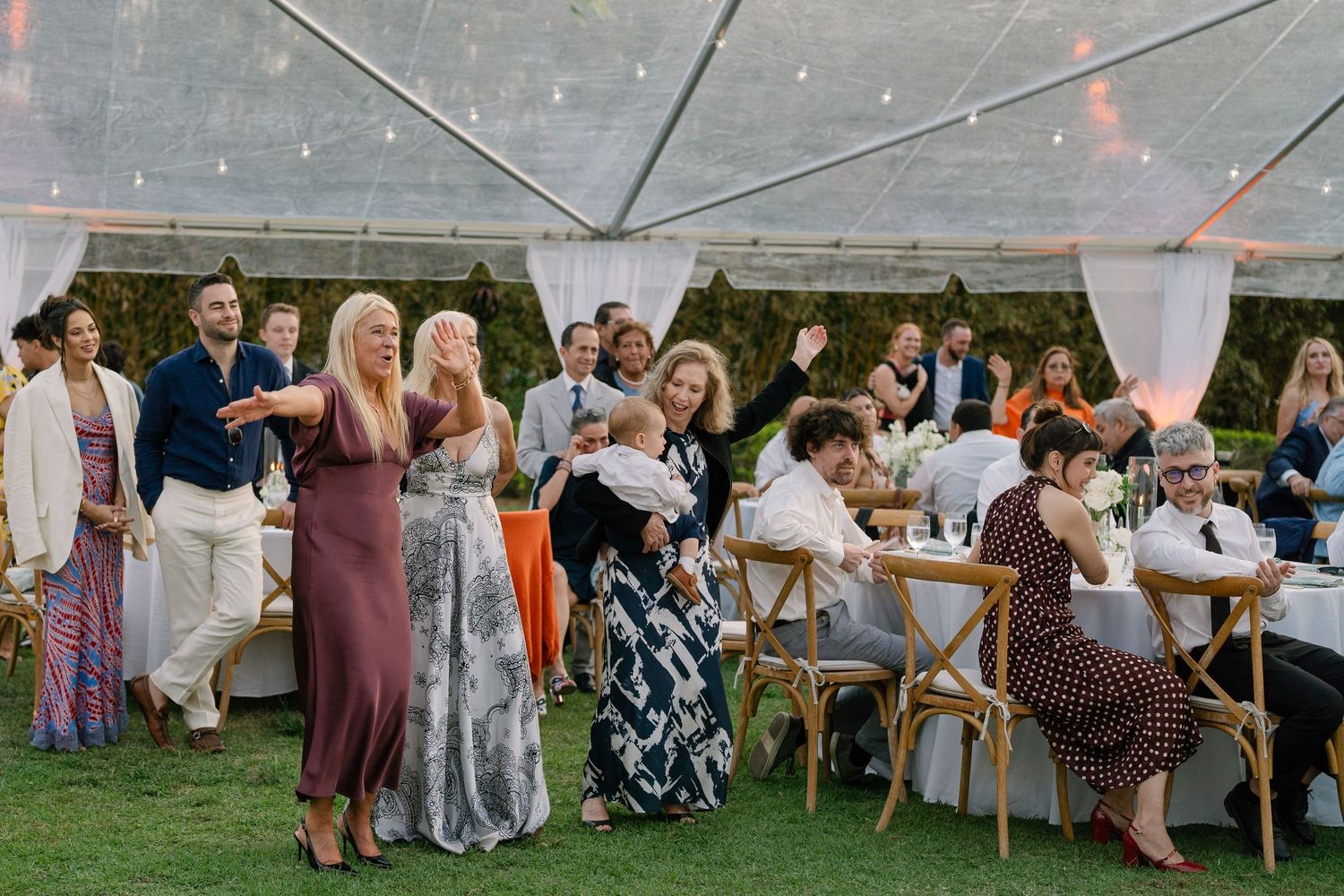 Wedding guests mingling and celebrating under a clear tent at a lively outdoor tropical wedding reception.