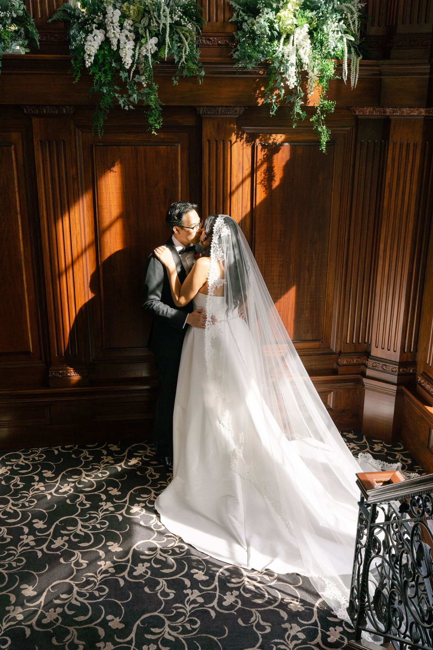 A romantic wedding photo shoot in a wood-paneled room with dramatic lighting and flowing white dress.