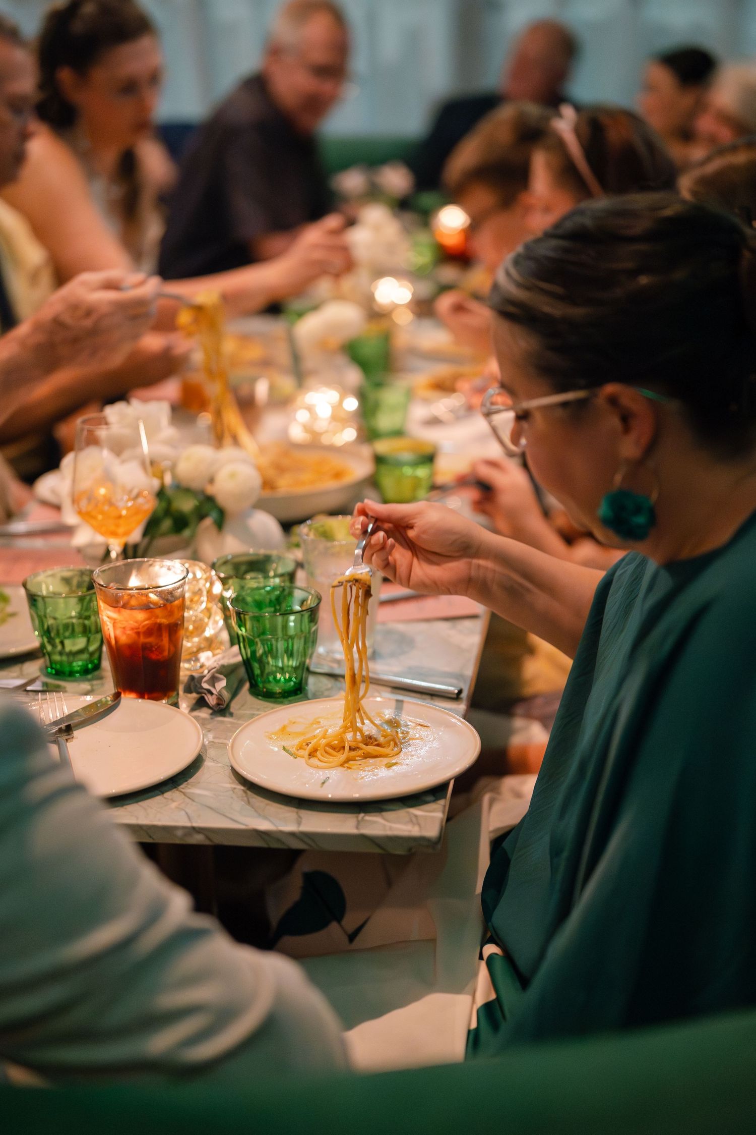 People enjoying dinner at a dimly lit table with colorful glassware and plated meals.