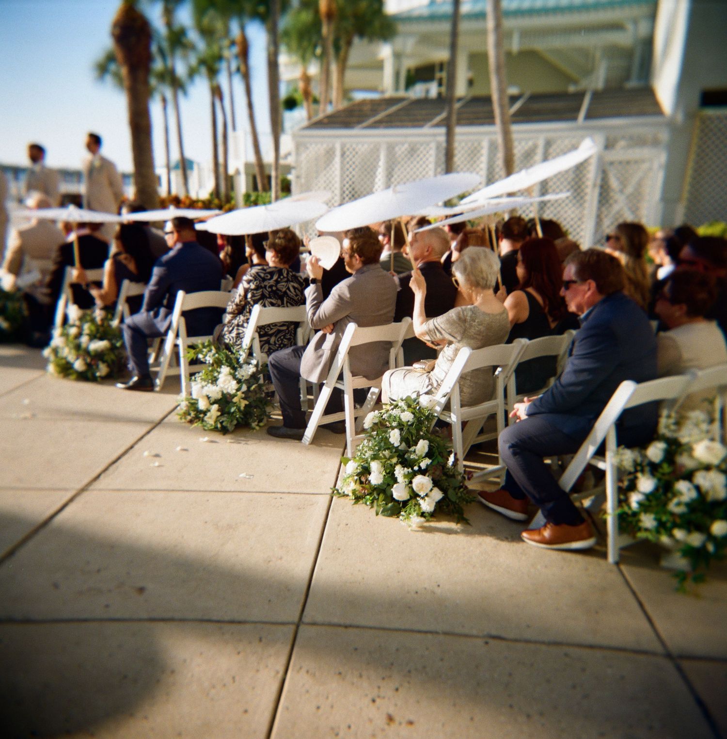 Wedding guests seated in white chairs at an outdoor waterfront ceremony.