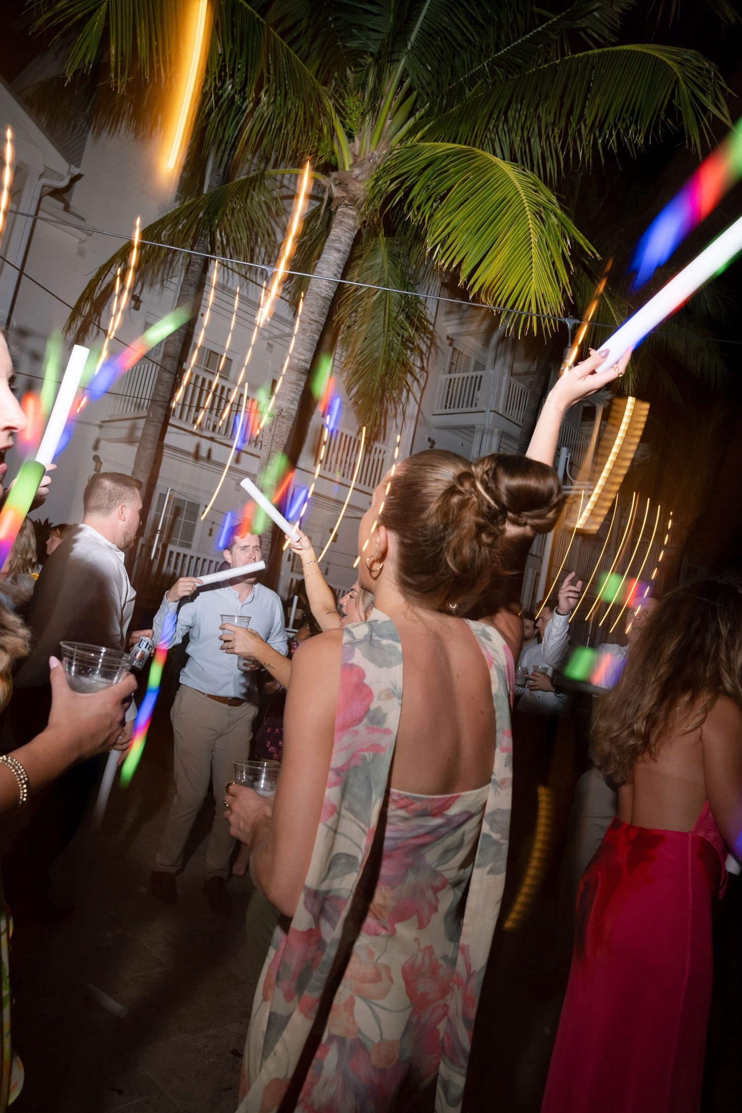 Wedding party guests dancing with colorful light-up wands during nighttime celebration.
