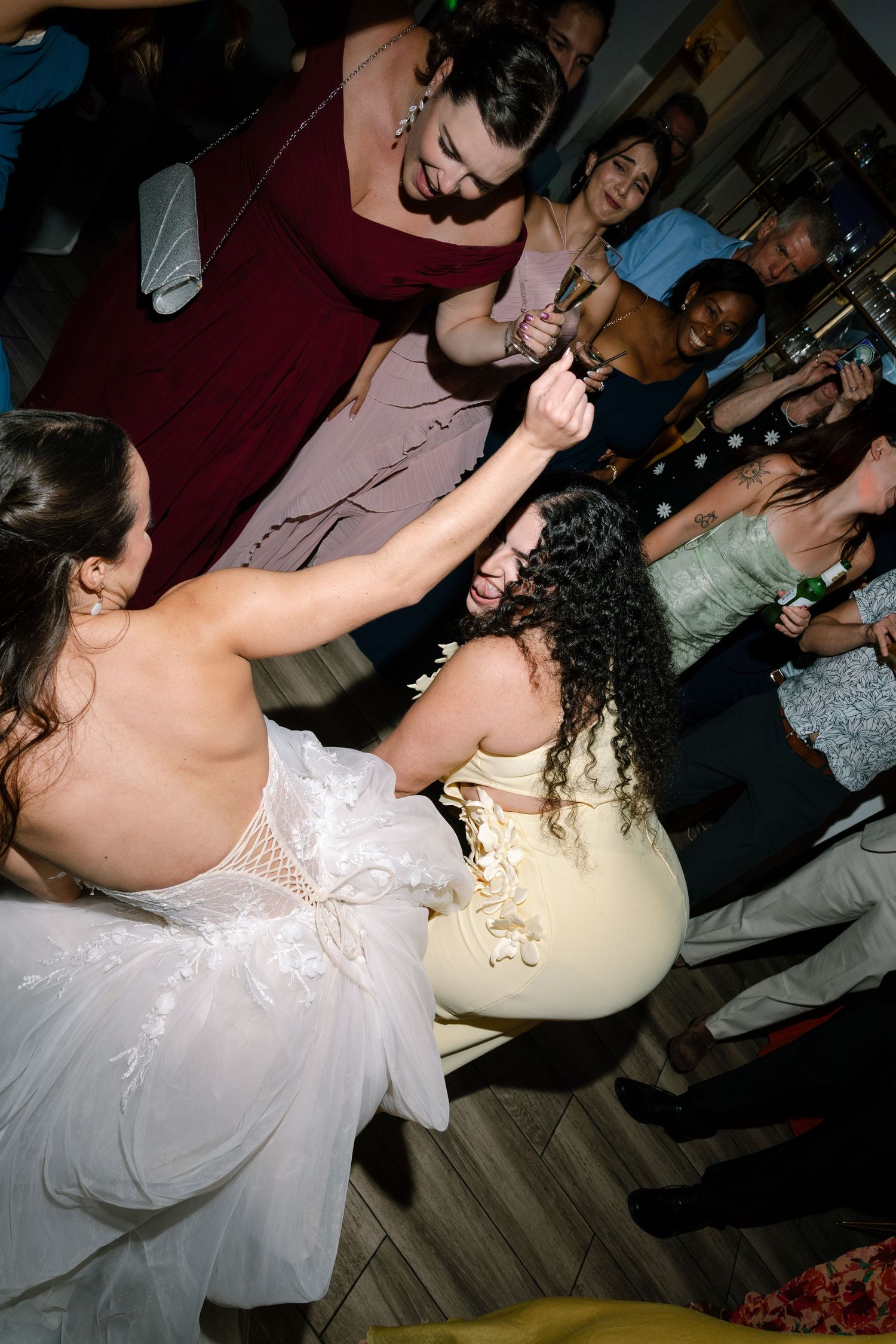 Bride in white gown dancing with guest in yellow dress at lively wedding reception celebration.
