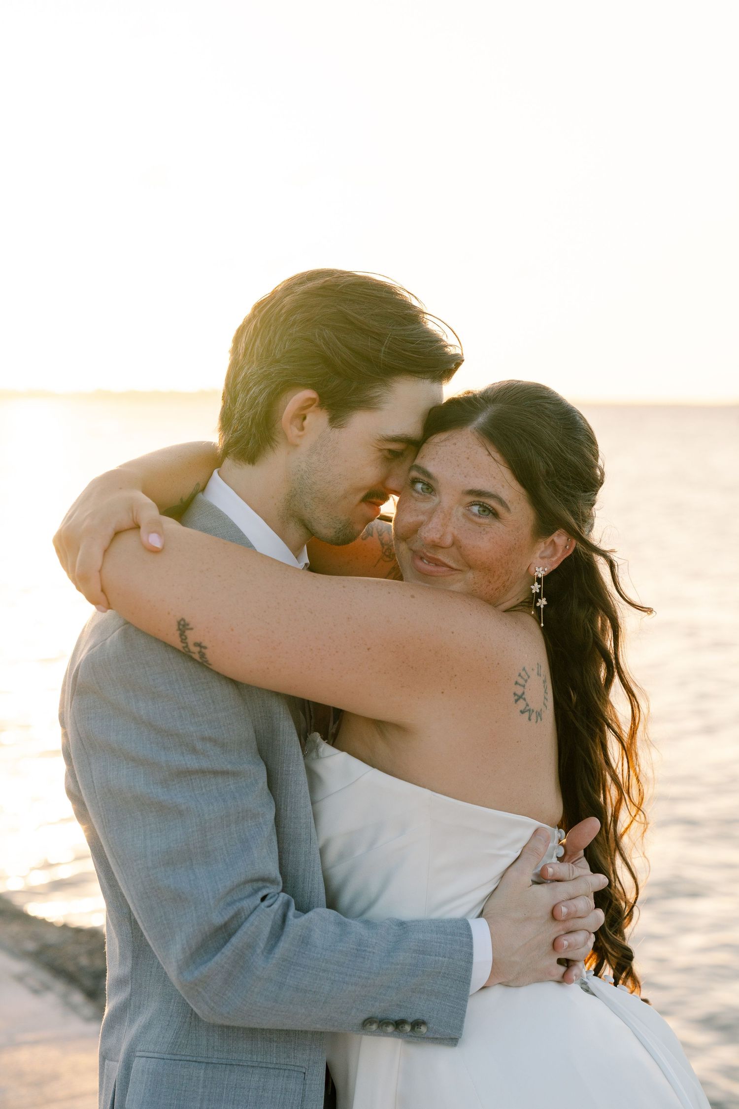 A man and woman embracing on a beach at sunset, with the ocean in the background.
