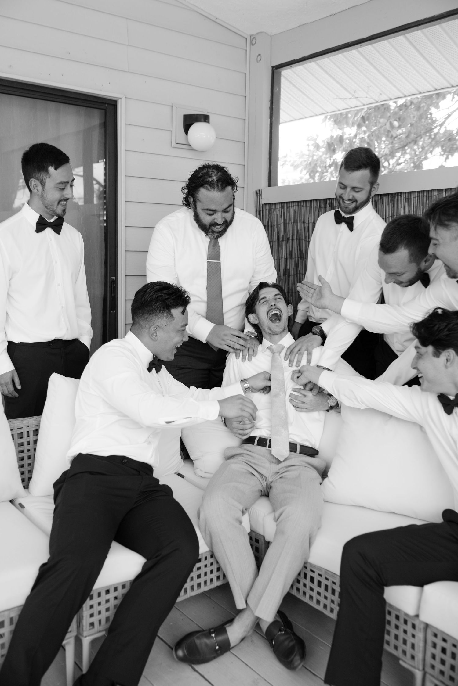 A group of men in formal attire, including tuxedos, are gathered together and appear to be celebrating or socializing.