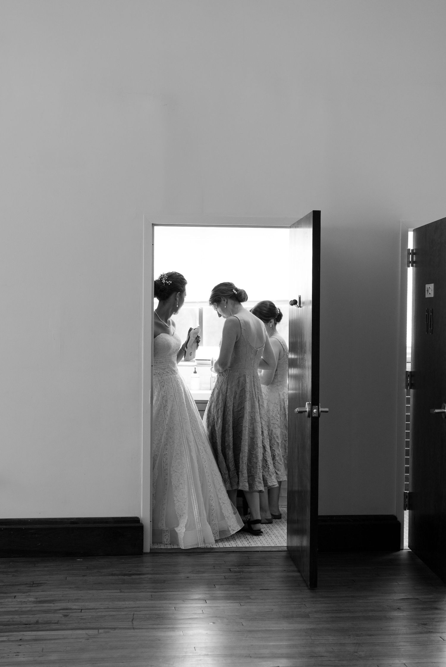Black and white silhouettes of formal dresses and gowns reflected in mirrors along a minimalist hallway.
