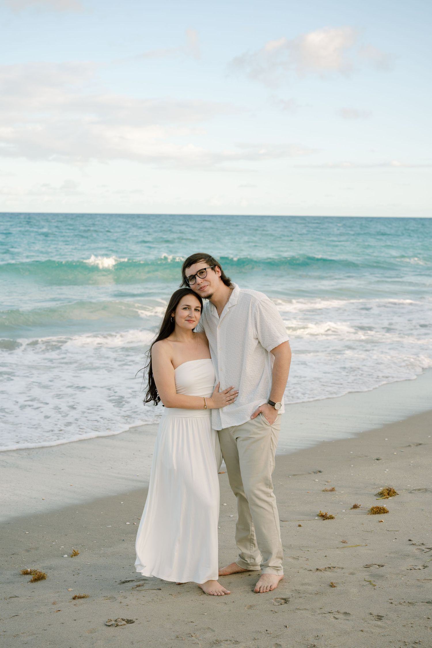 A couple shares a romantic moment together on a sandy beach with turquoise ocean waves in the background.