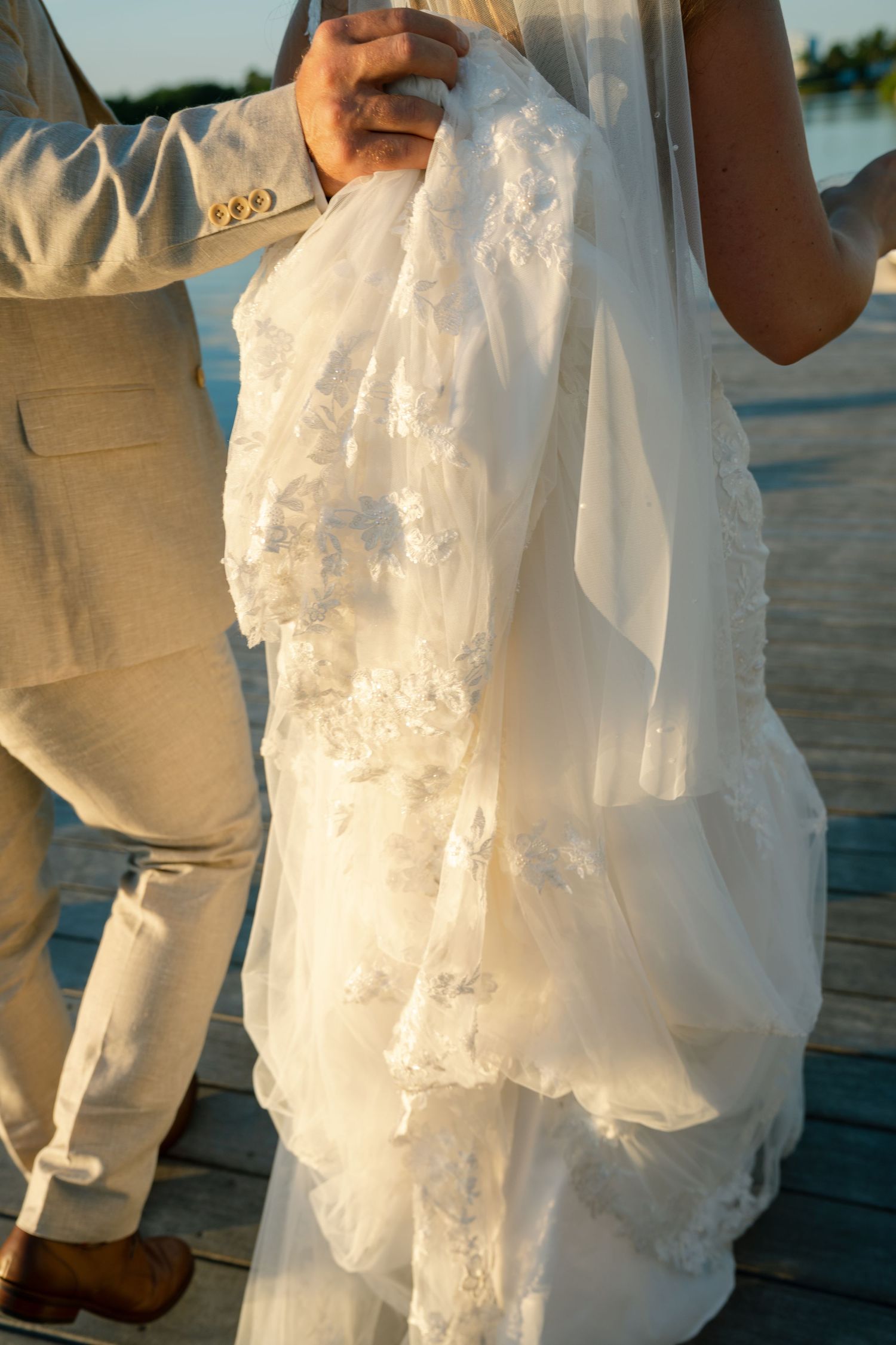 Close-up detail of a white lace wedding dress and khaki suit during an outdoor ceremony.