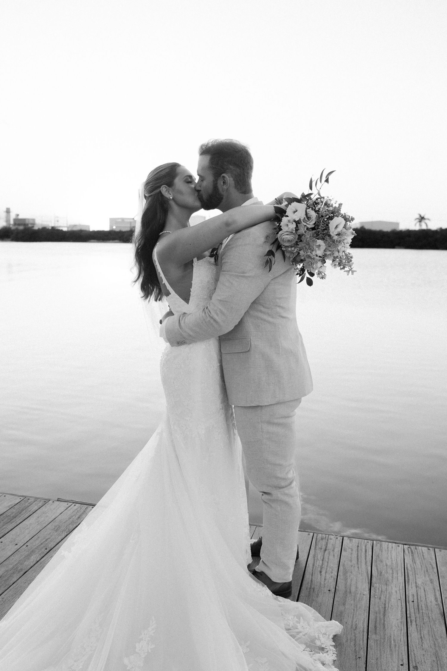 Wedding couple sharing romantic kisses on a dock by the water in black and white.