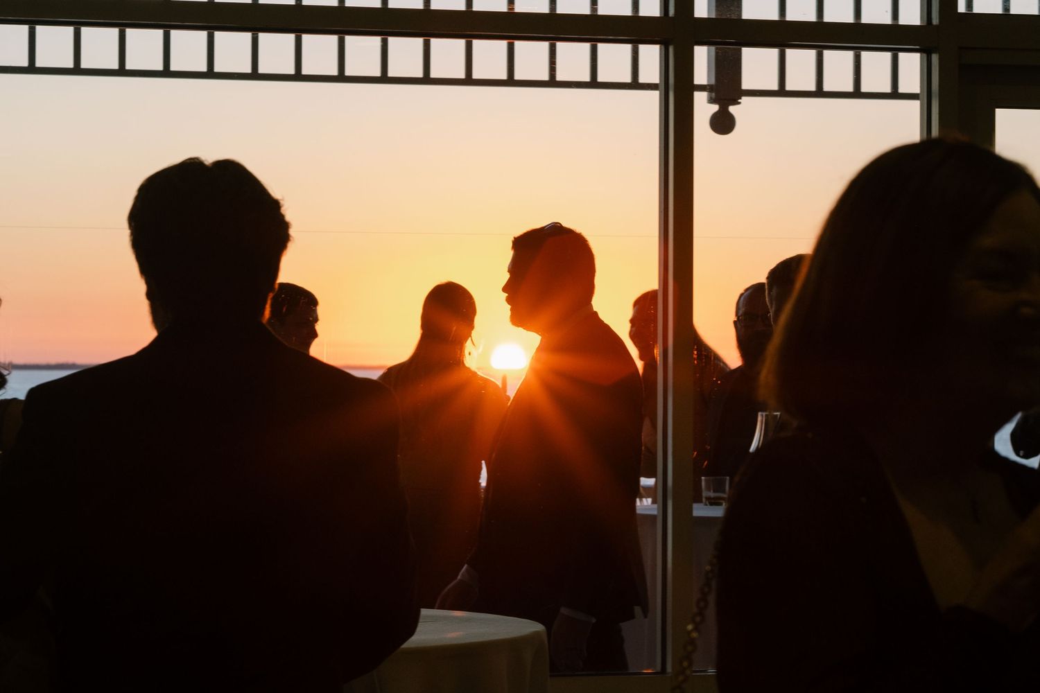 Silhouettes of people against a dramatic sunset through large windows.