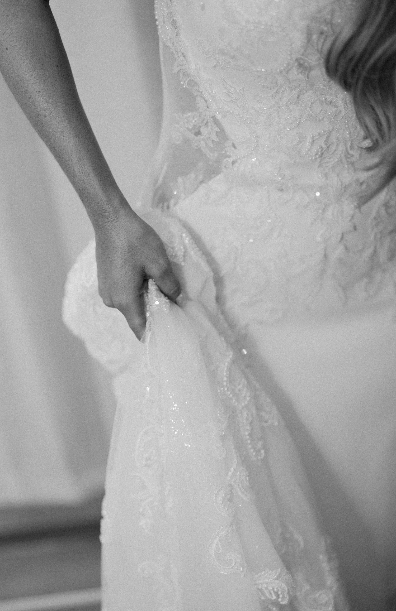 Black and white detail shot of a hand grasping delicate lace on a wedding dress.