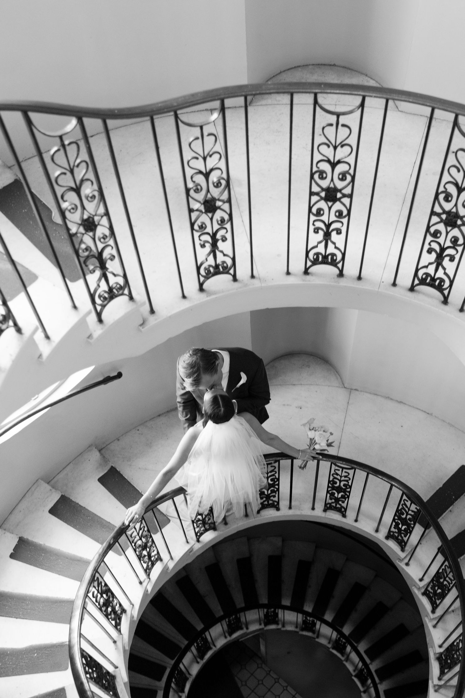 Black and white aerial view of a bride and groom sharing a romantic moment on an elegant spiral staircase.