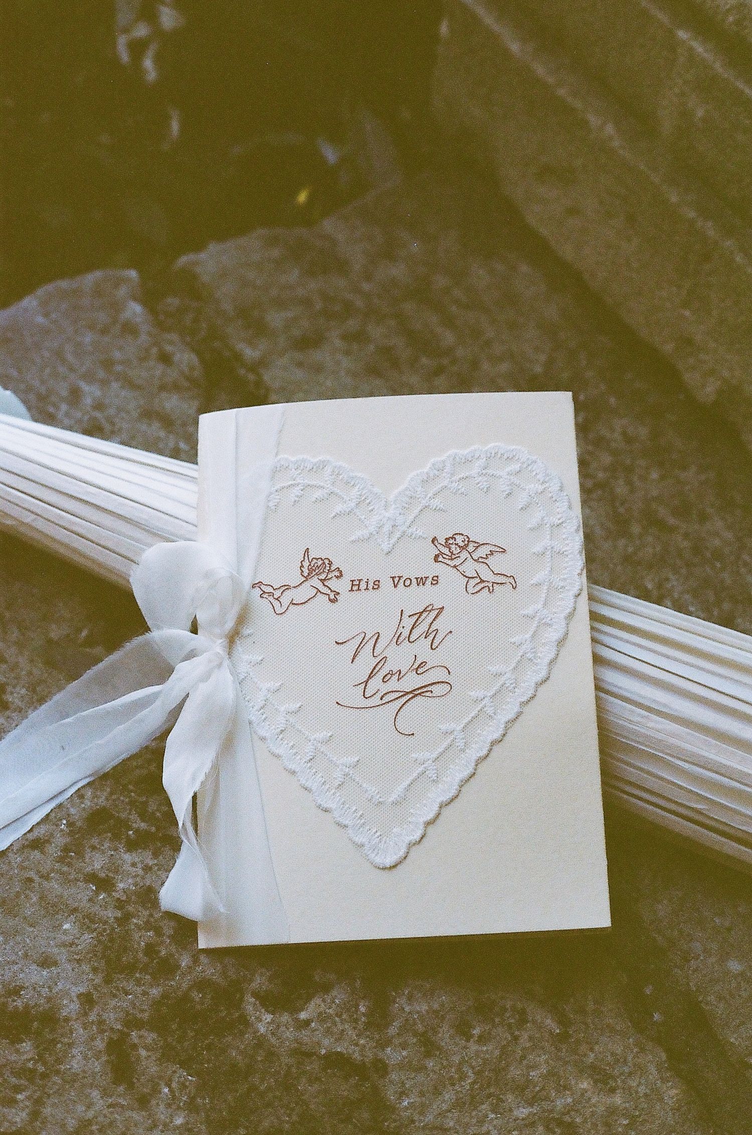 Elegant wedding vow booklet with heart lace design and cherubs tied with white ribbon bow.