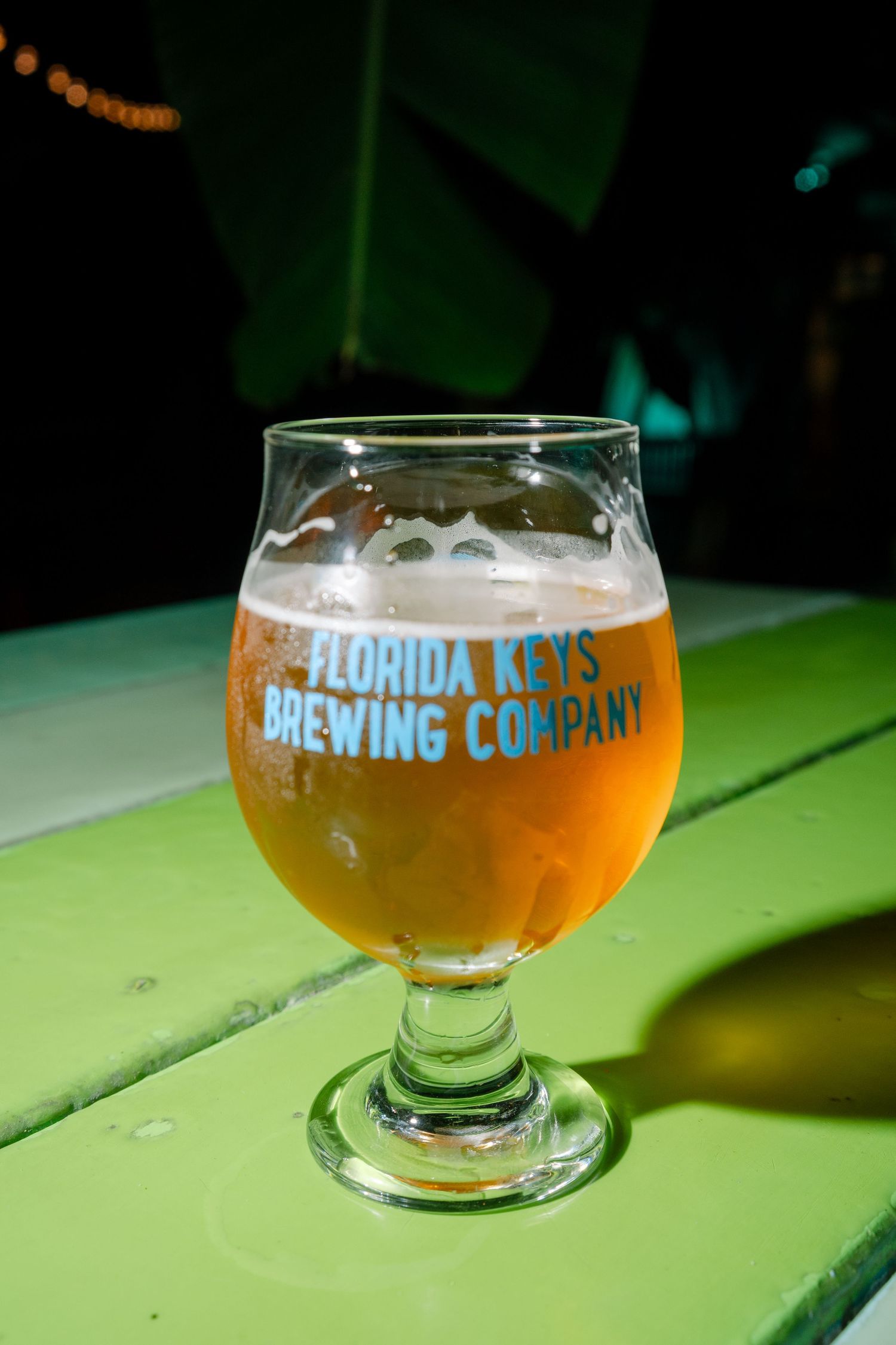 Florida Keys Brewing Company beer glass filled with golden ale on green wooden surface.