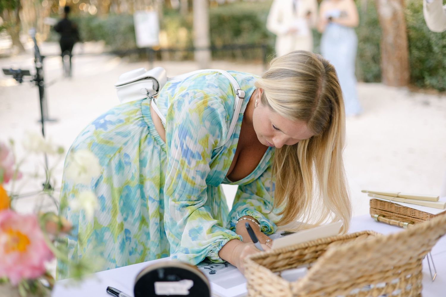 Someone in a floral print dress arranges items on a rustic wooden table at an outdoor event.