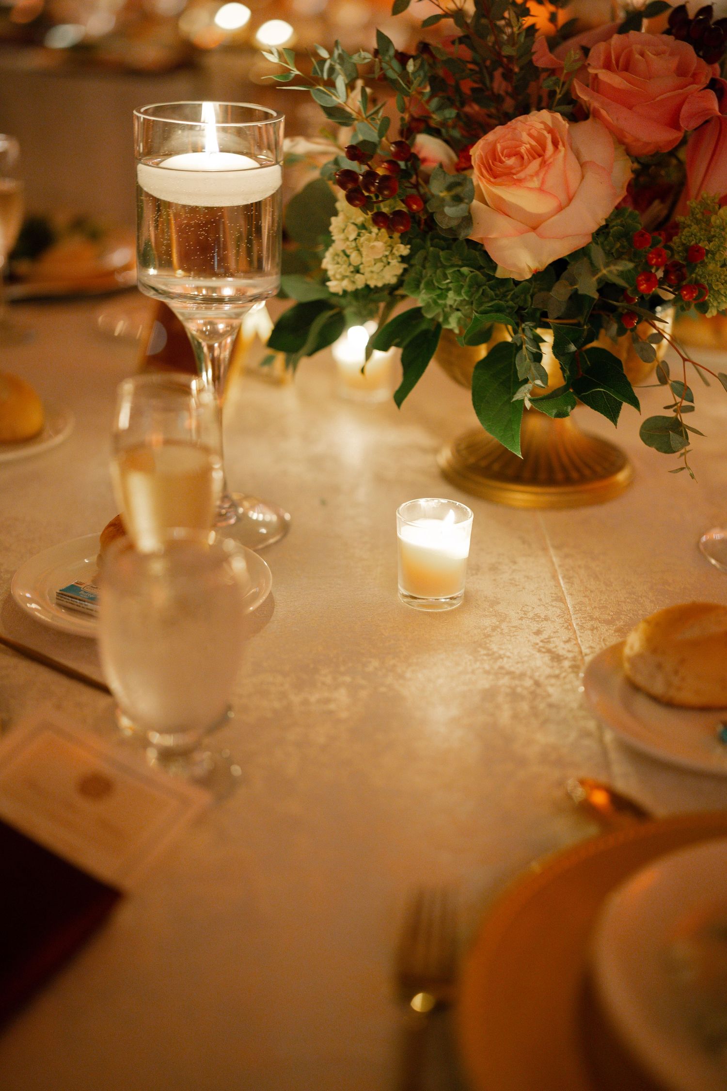Romantic wedding reception table setting with soft candlelight, peach roses and glassware.