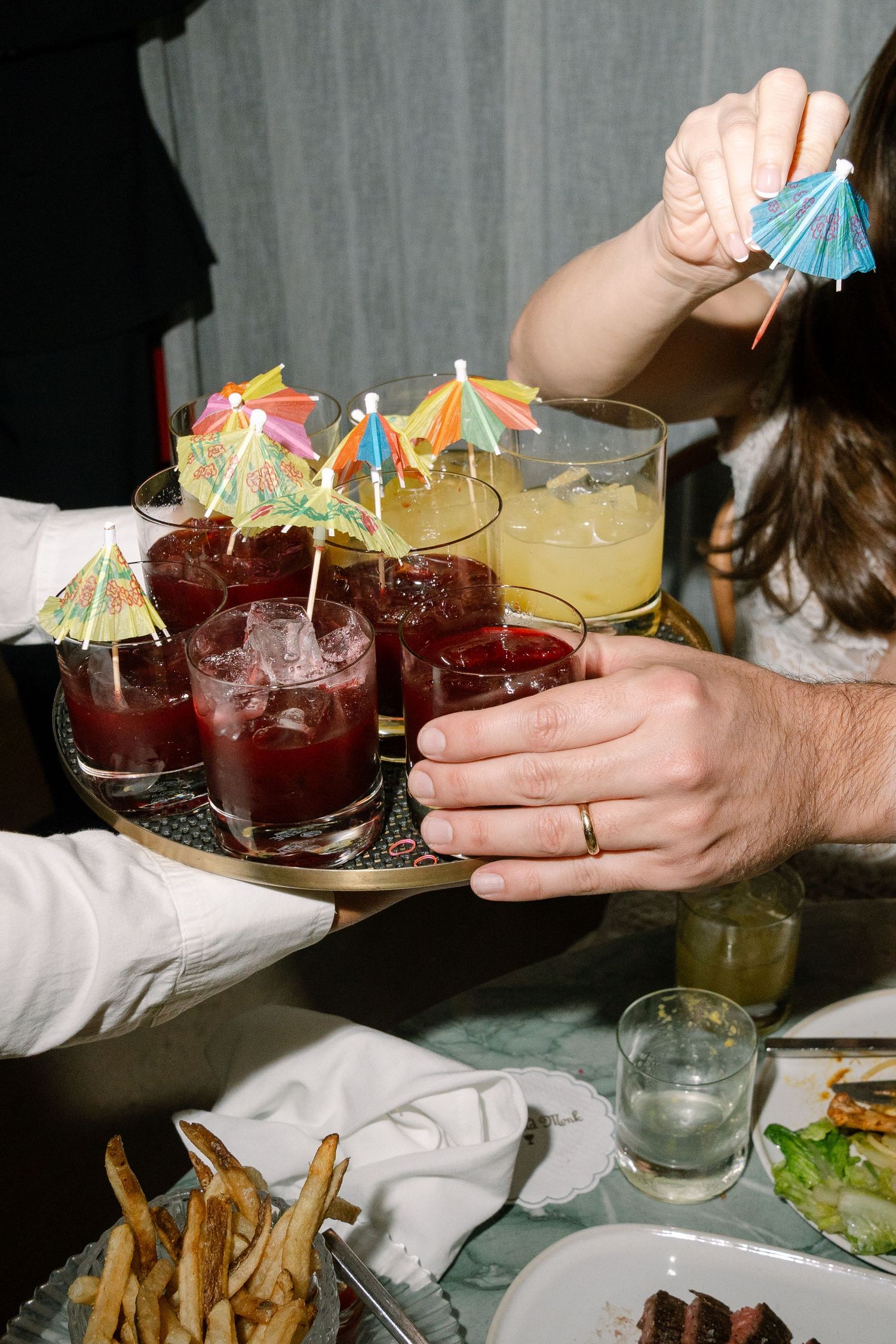 Colorful cocktails with umbrella garnishes and french fries are served at a restaurant table.