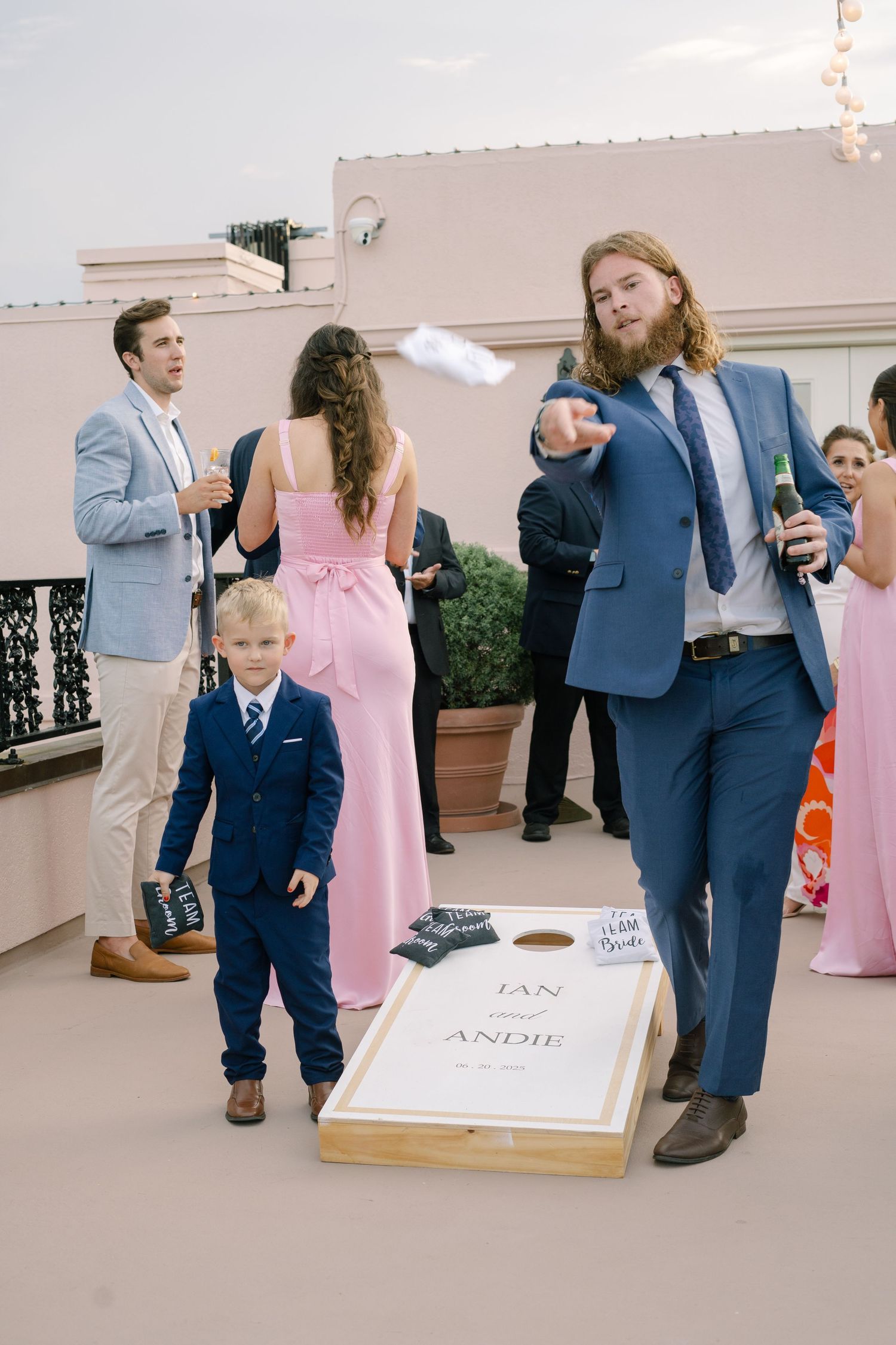 Wedding guests playing cornhole on a rooftop during a reception with string lights.