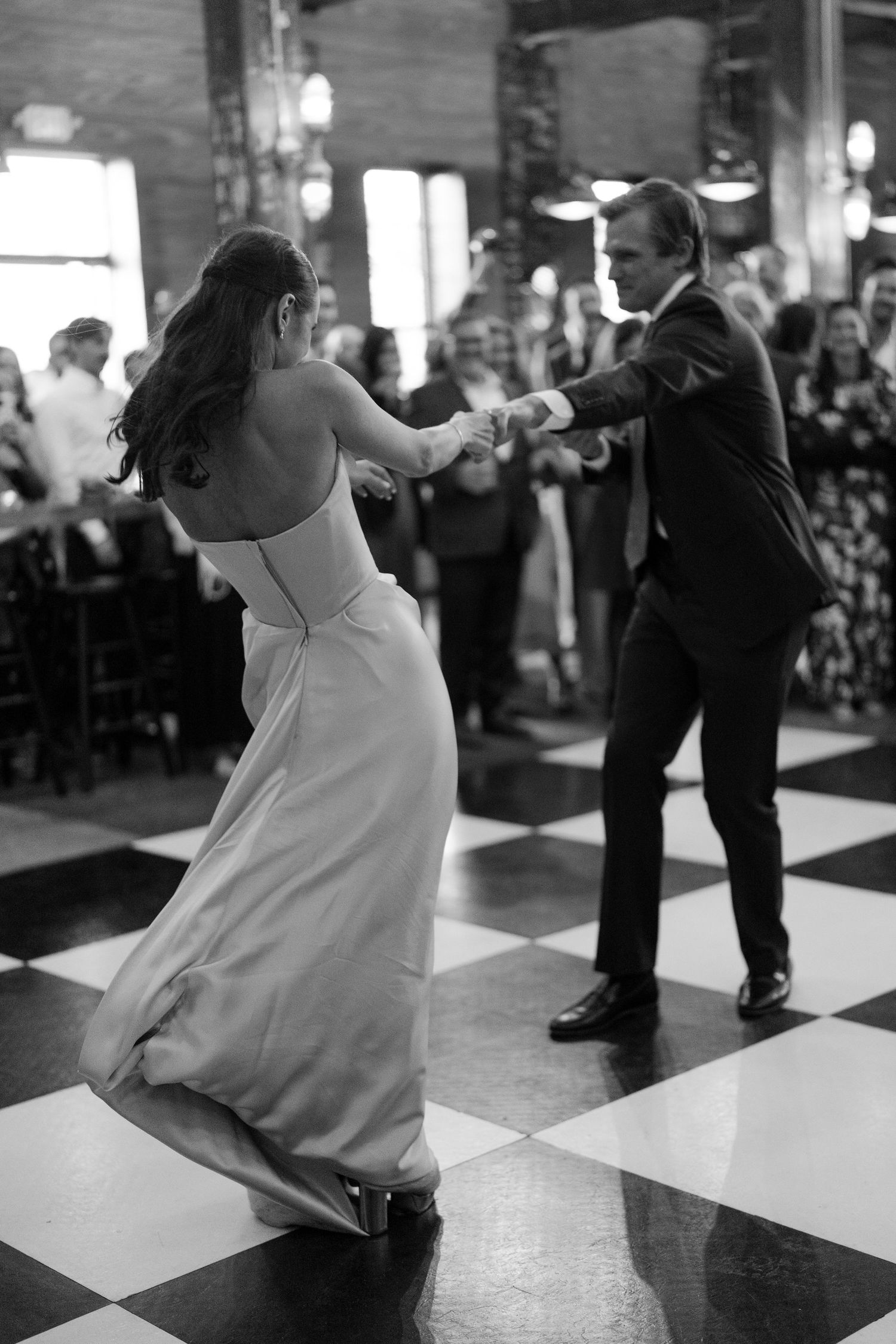 Bride and groom share first dance on checkered floor in black and white wedding reception photo.