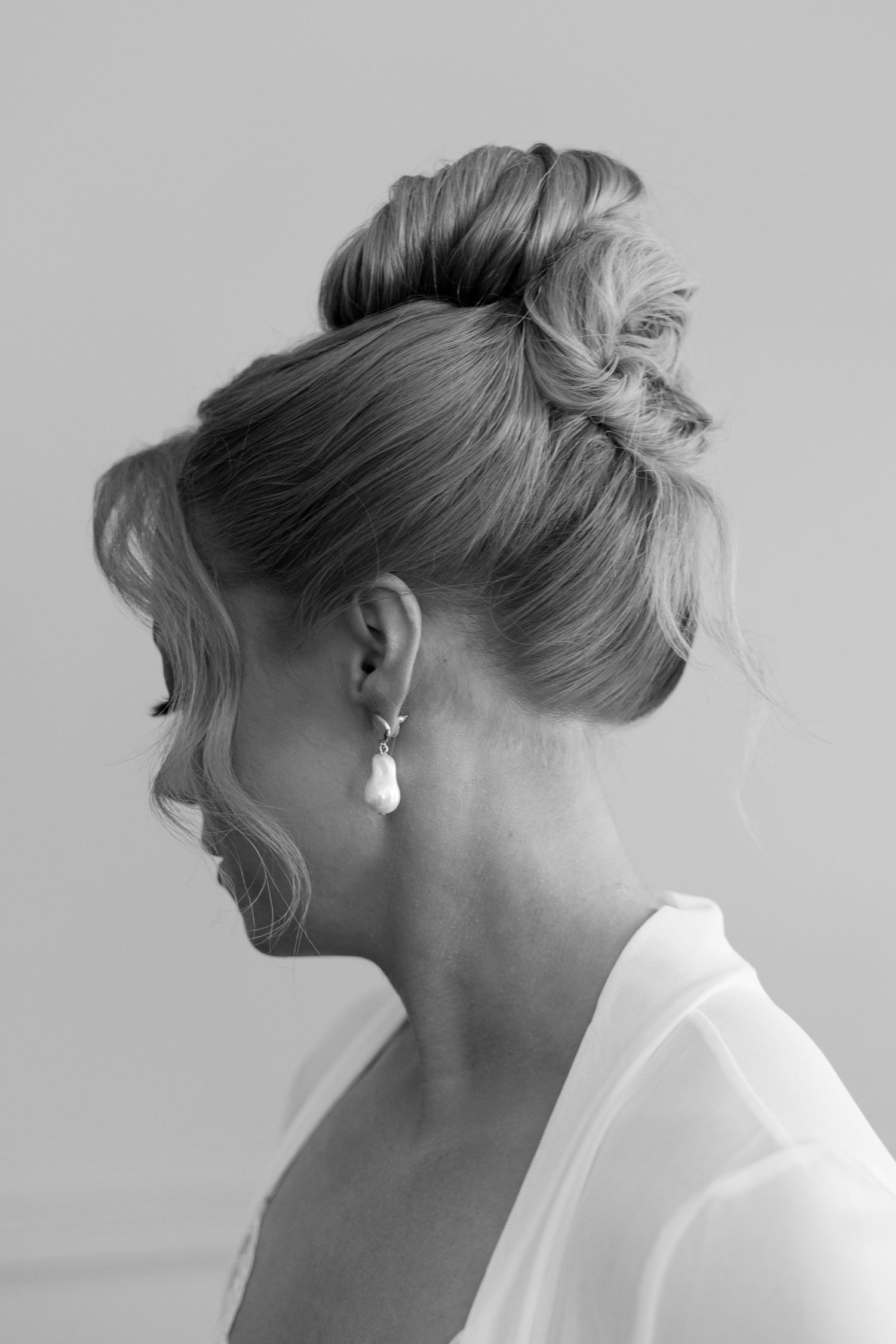 Profile views of an elegant updo hairstyle with pearl earrings in black and white.