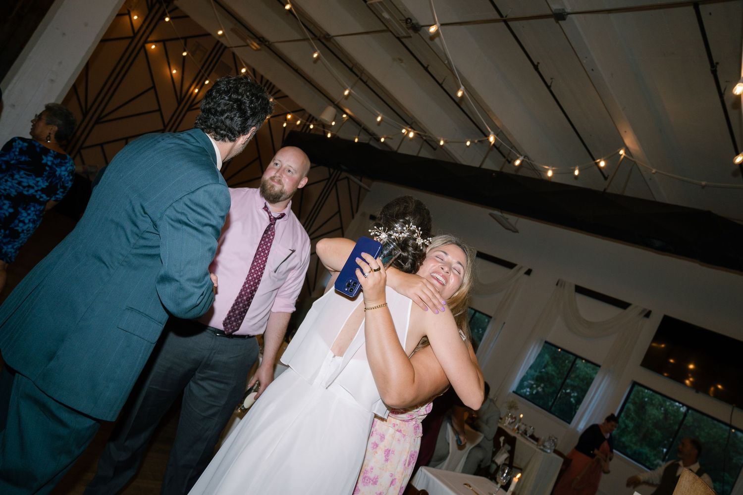 Wedding guests celebrate on the dance floor under string lights in a reception venue.