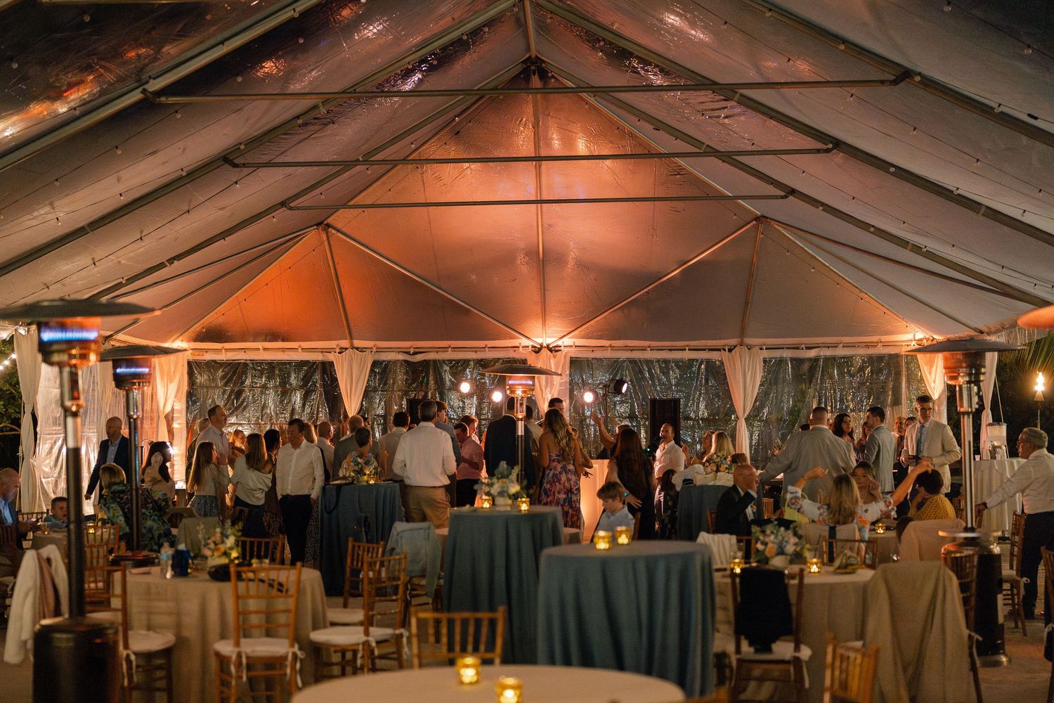 Evening wedding reception in a large illuminated tent with guests dining.
