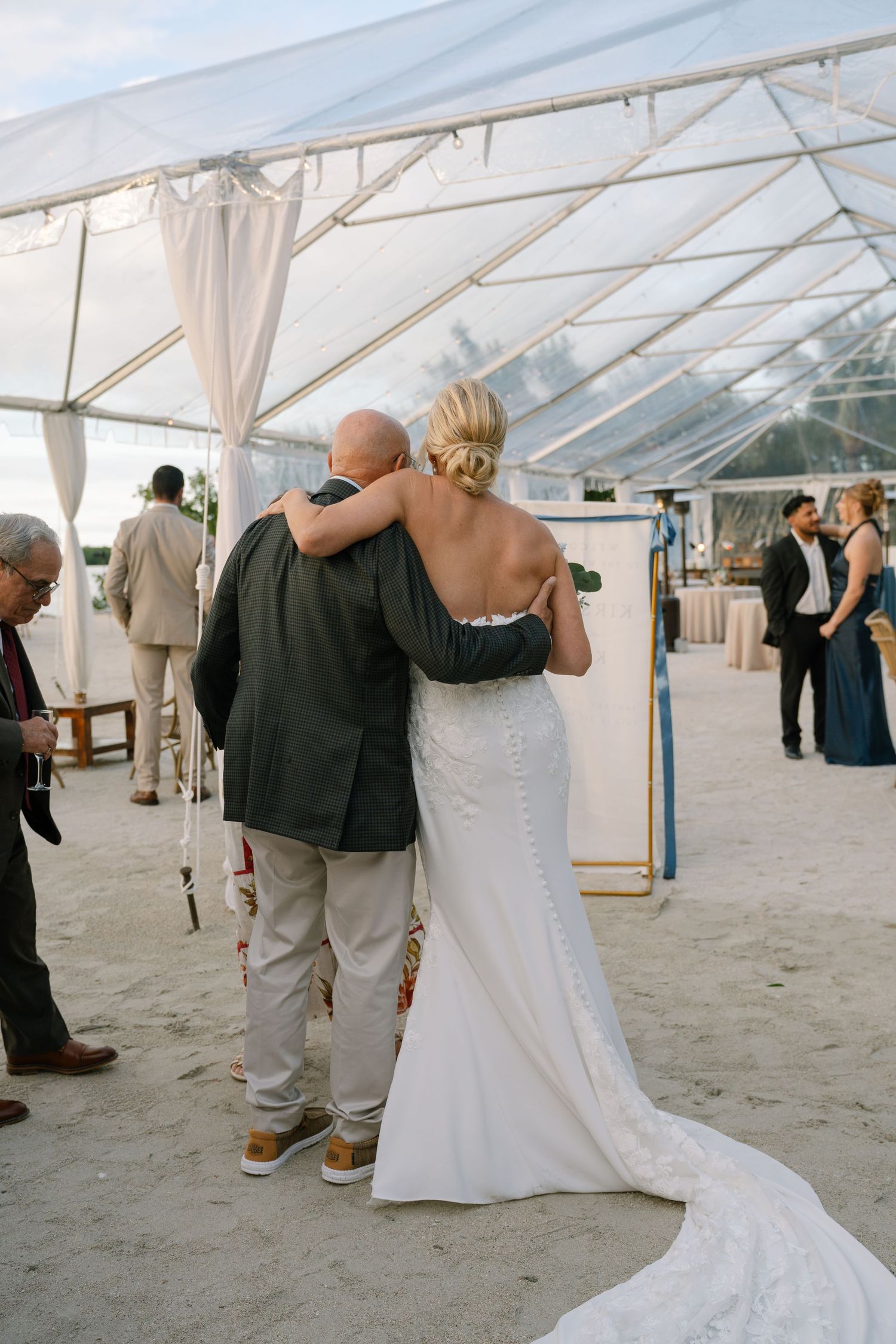 A tender moment shared under a clear-top tent during a wedding reception.