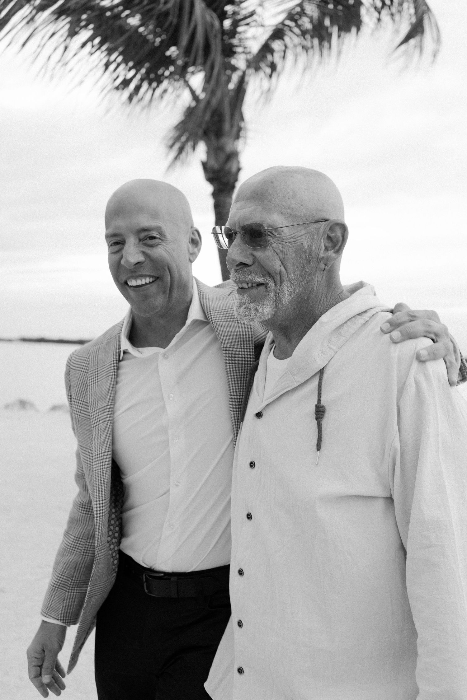 Three men in white shirts share joyful laughter while standing together outdoors in black and white photography.