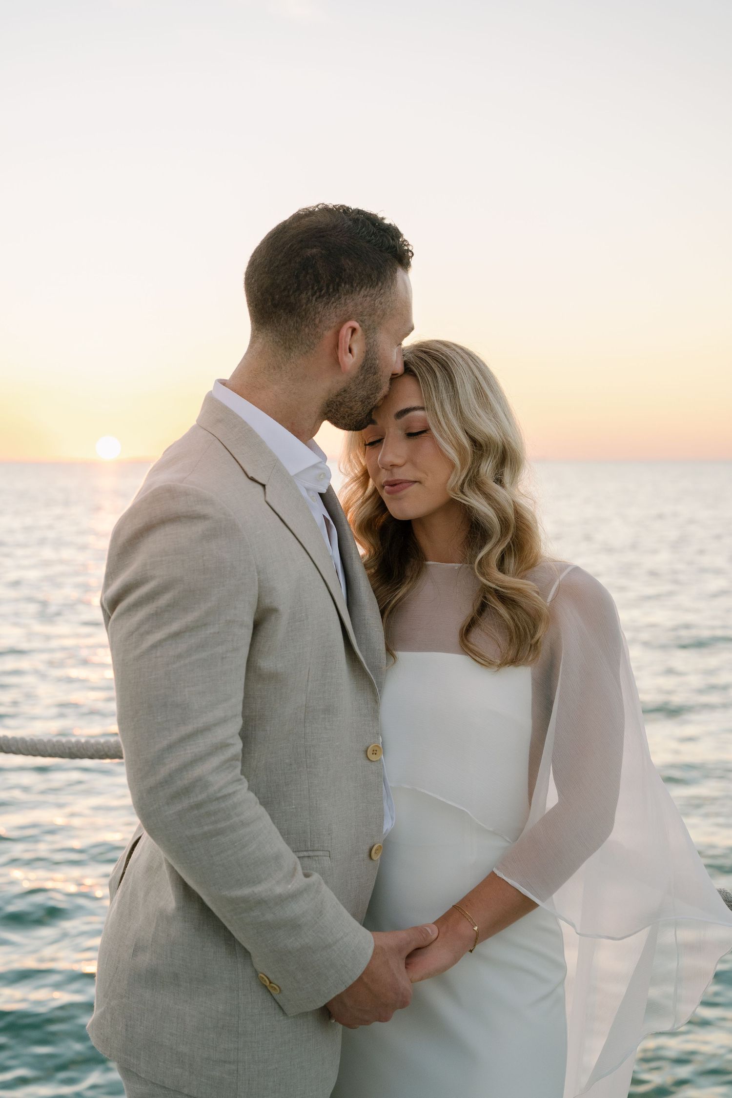 Intimate sunset portrait of couple in formal attire embracing by the ocean.
