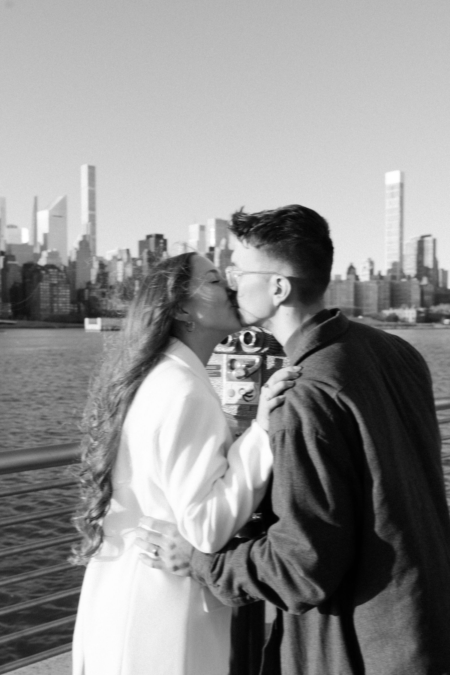 Couple in casual wear admiring Manhattan skyline from waterfront viewing area.