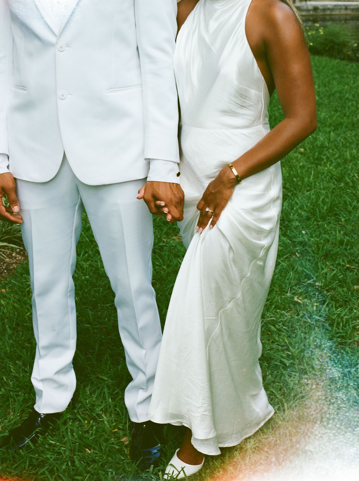 A group wearing all-white outfits stands together on a grassy lawn, showing only their legs and lower bodies.