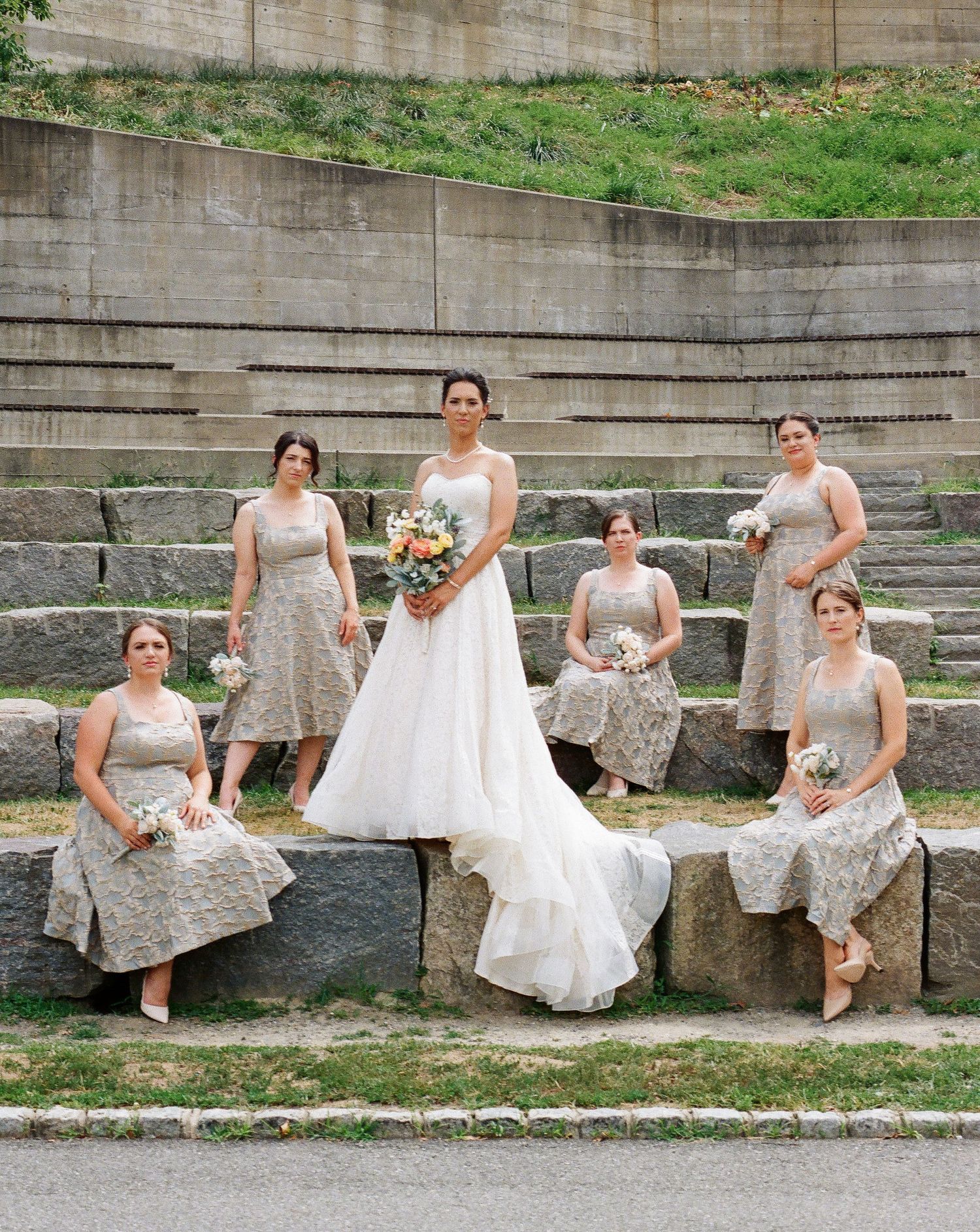 Bridesmaids in matching dresses posed on stone steps in an amphitheater setting.