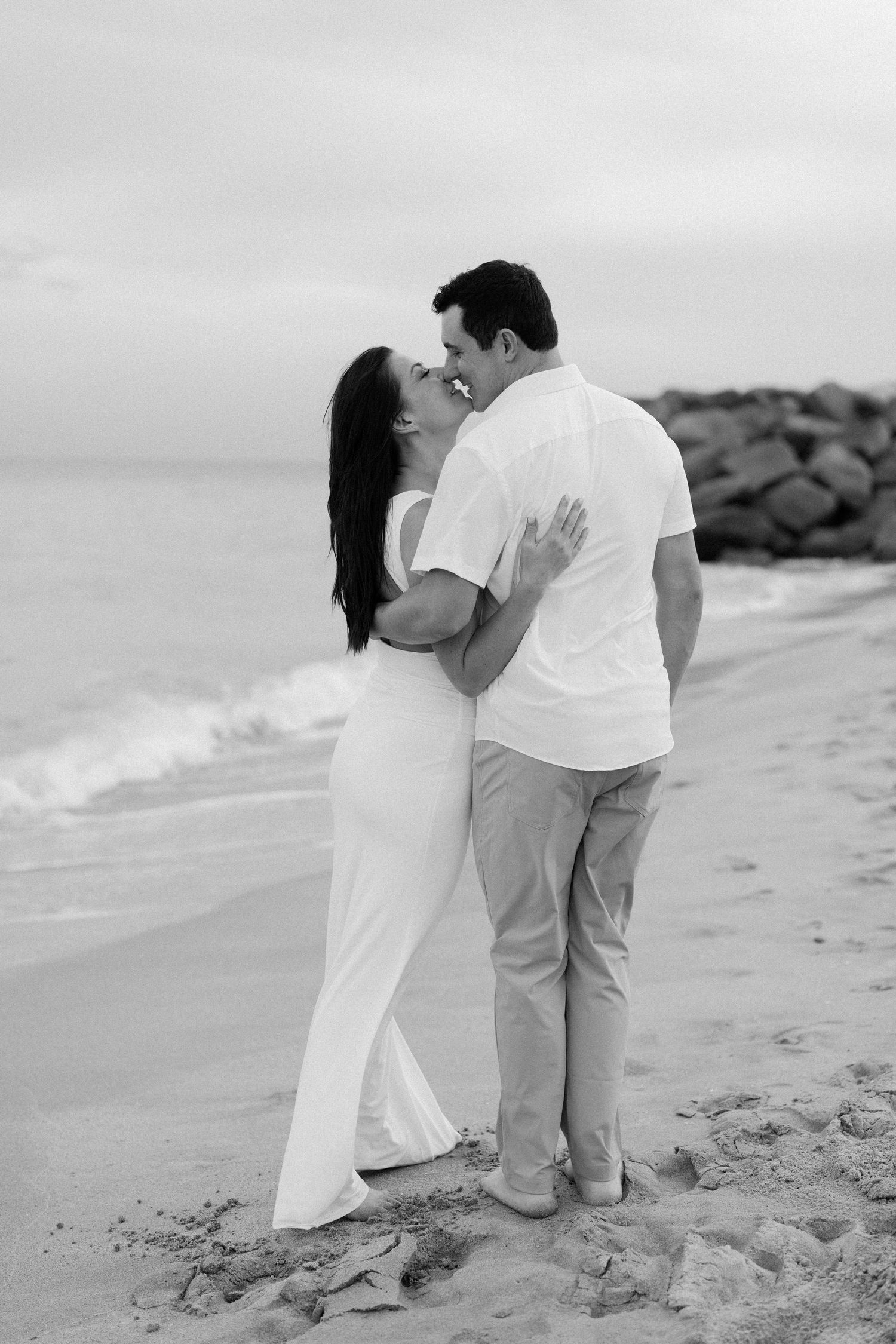 A couple shares romantic moments on a sandy beach with waves in the background.