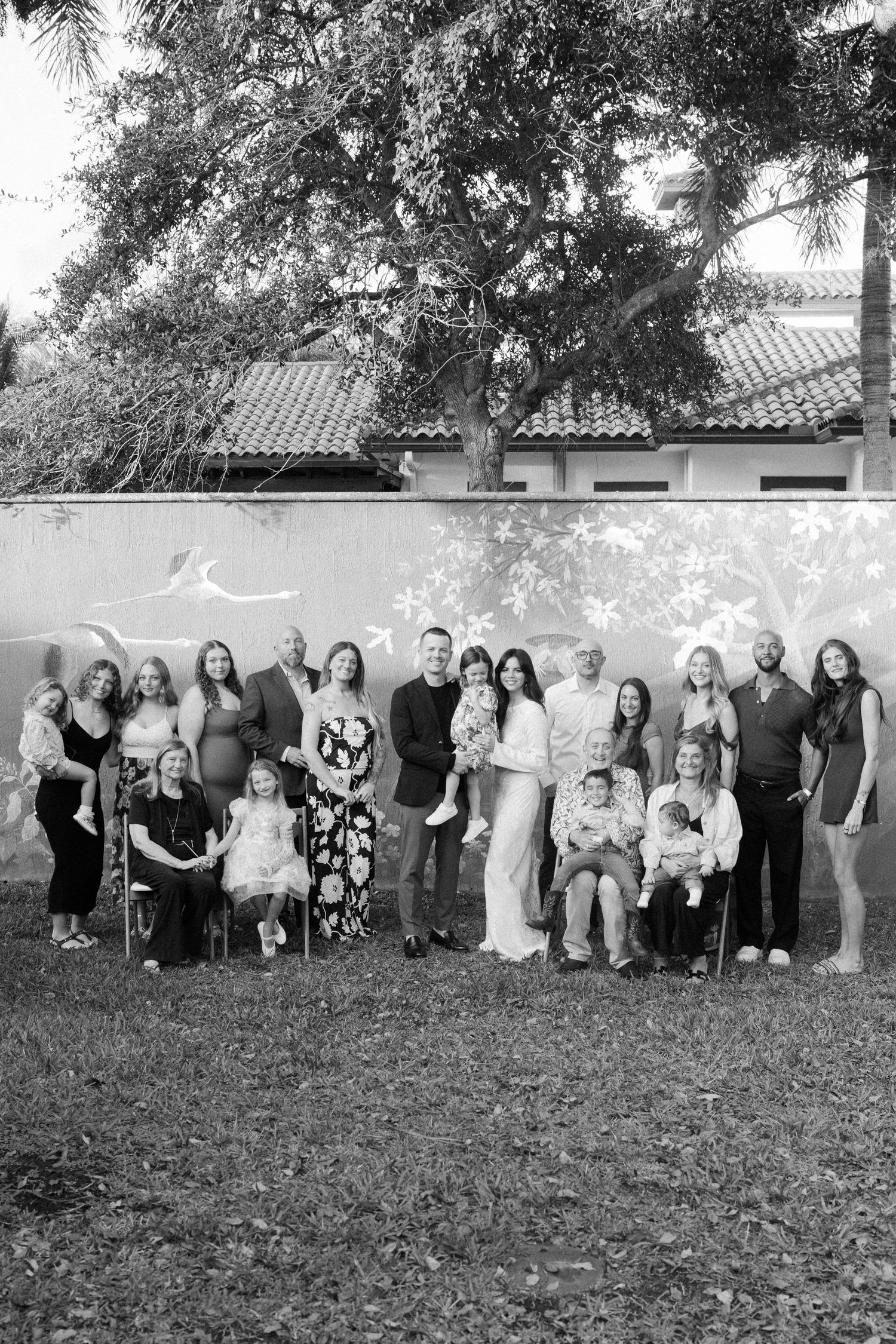 Large group photo of wedding guests arranged in a line outdoors in black and white.
