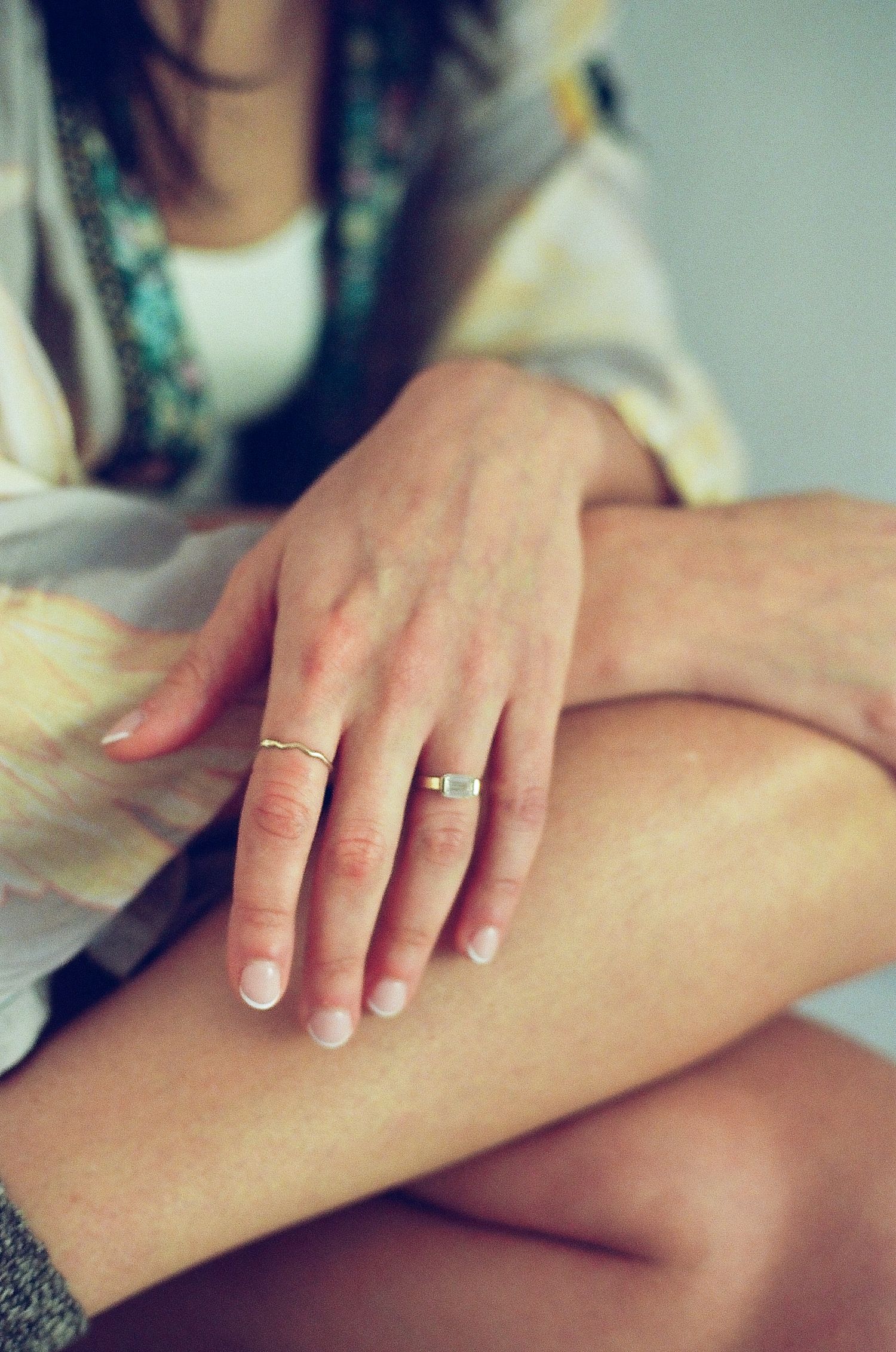 Close-up of a woman's hand with an engagement ring resting on her bare leg.