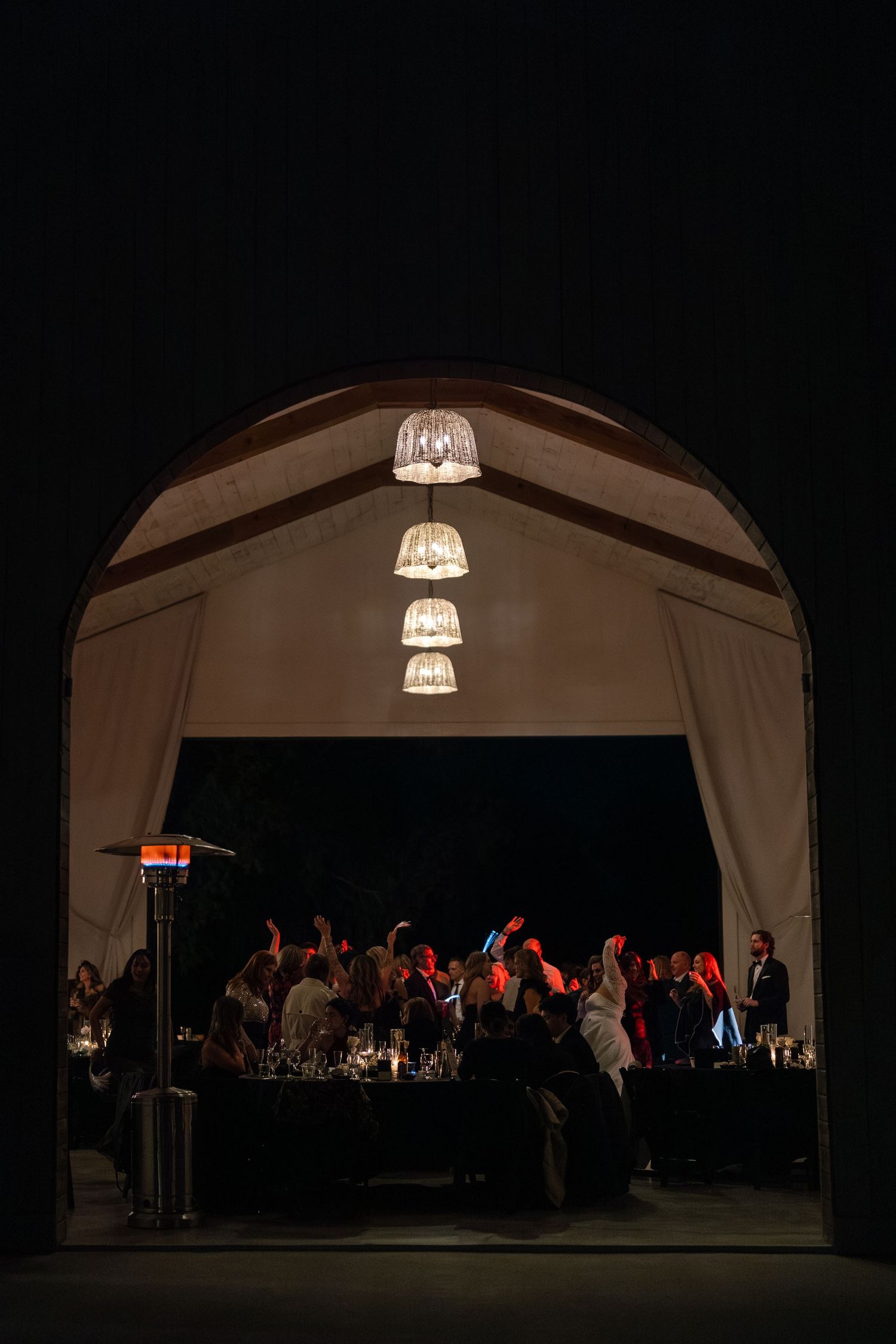 A large crowd gathered in a dimly lit indoor venue, with hanging lights illuminating the scene.