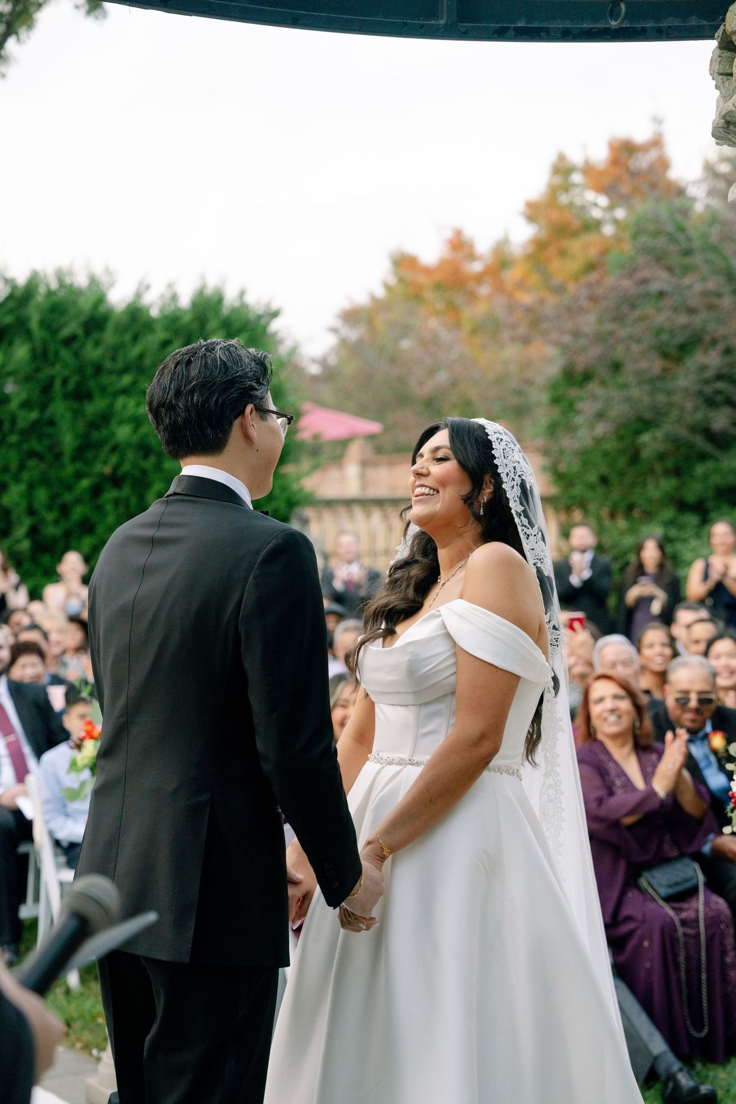 A joyful wedding ceremony outdoors with guests watching as the couple shares a happy moment in autumn.