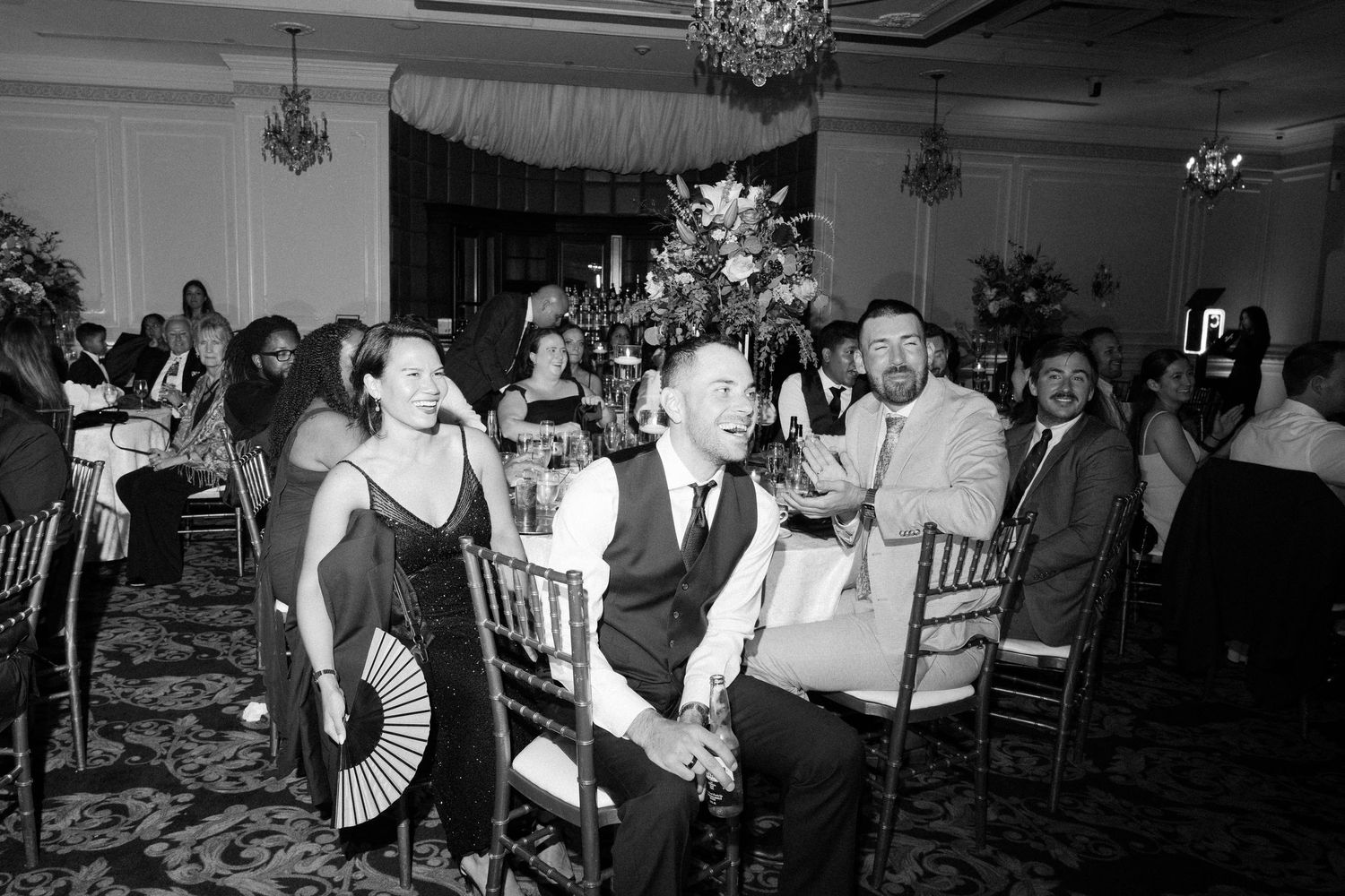 Black and white photo of wedding guests dancing and celebrating at an indoor reception.