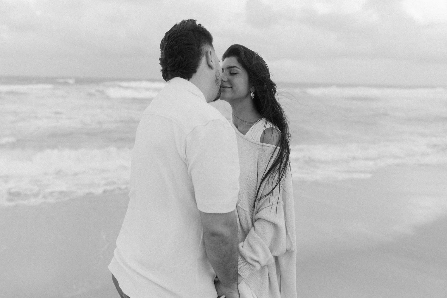 A romantic couple embraces on a serene beach in black and white photography.