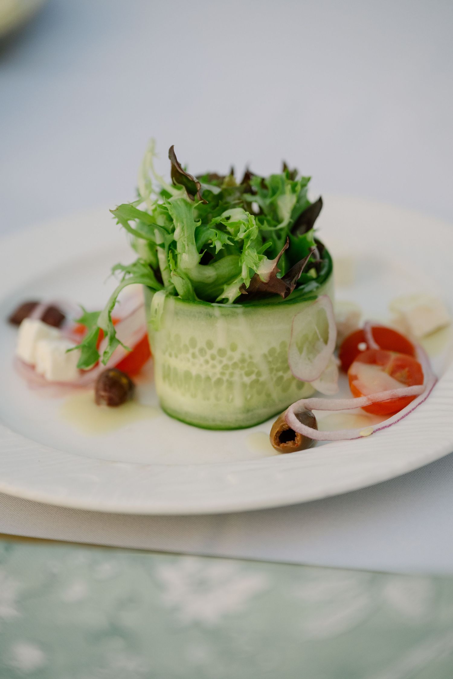 Elegant plated salad with fresh greens, tomatoes, cucumber, and olives served at a wedding reception.
