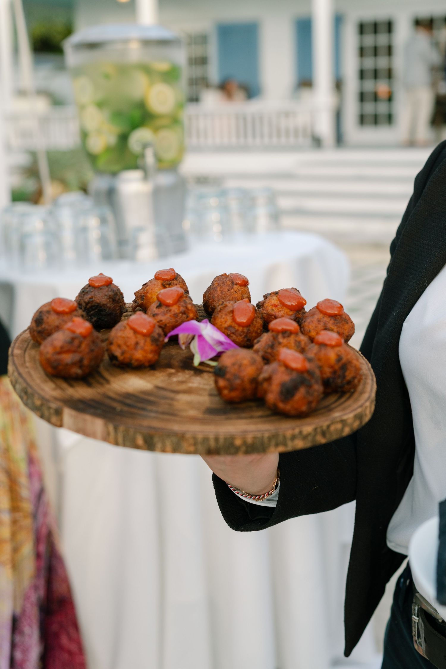 A wooden platter of appetizers being served at an outdoor wedding reception.