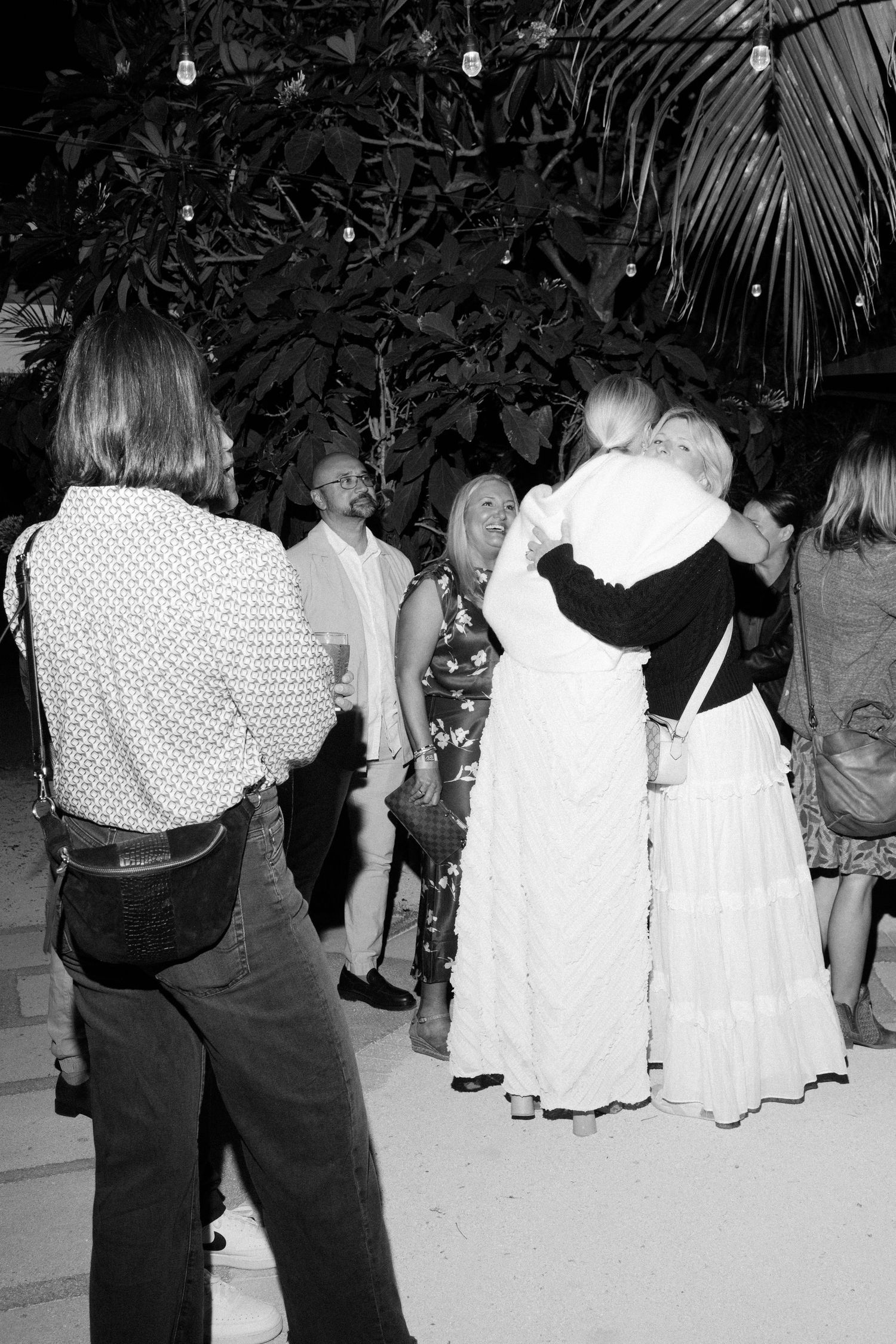 Group of people dancing at a party wearing white dresses and dark pants.