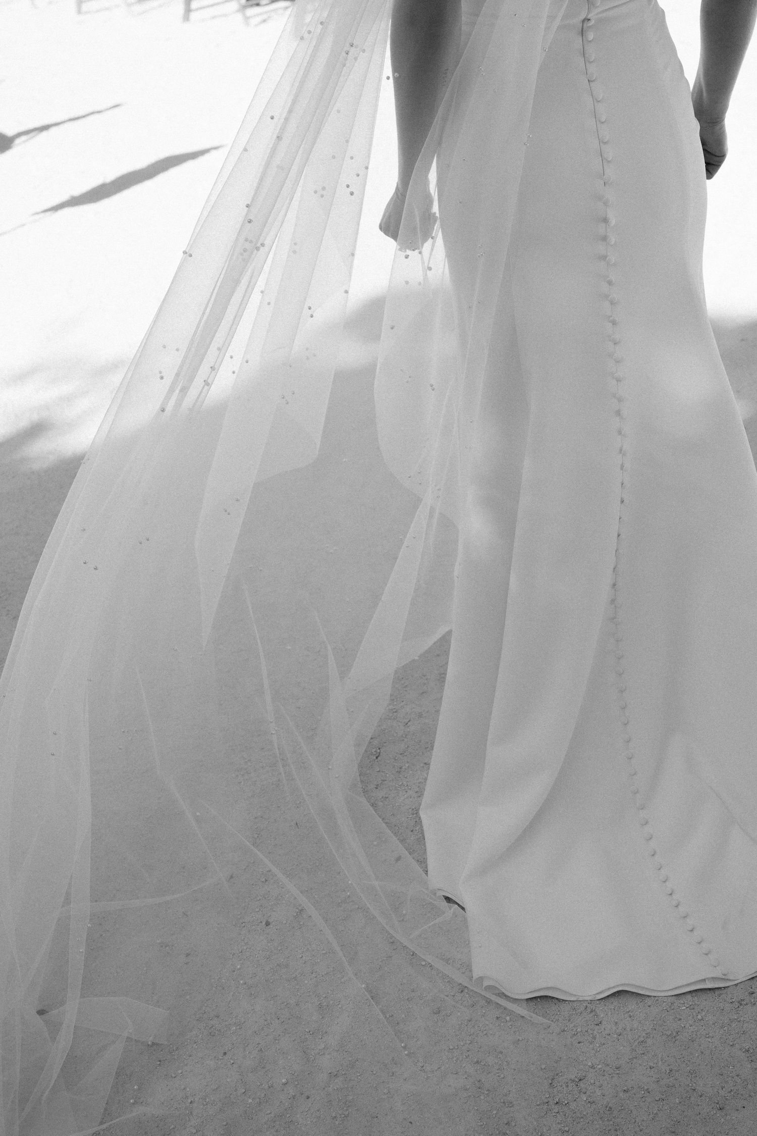 Black and white image of a flowing wedding dress train trailing on the ground.
