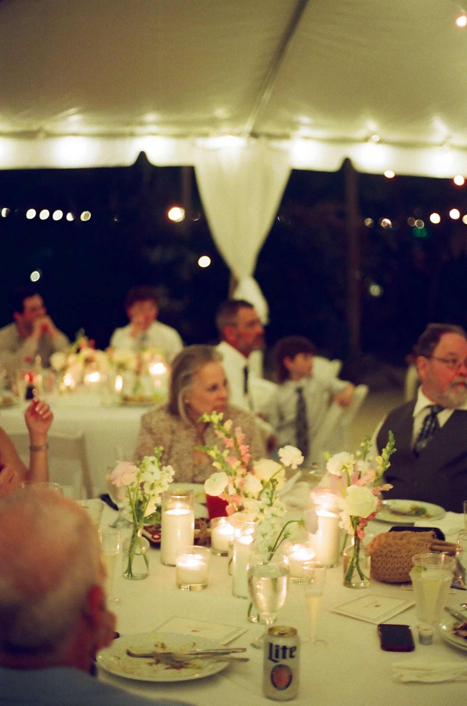 A formal dinner event with people seated at tables, surrounded by decorations and string lights.