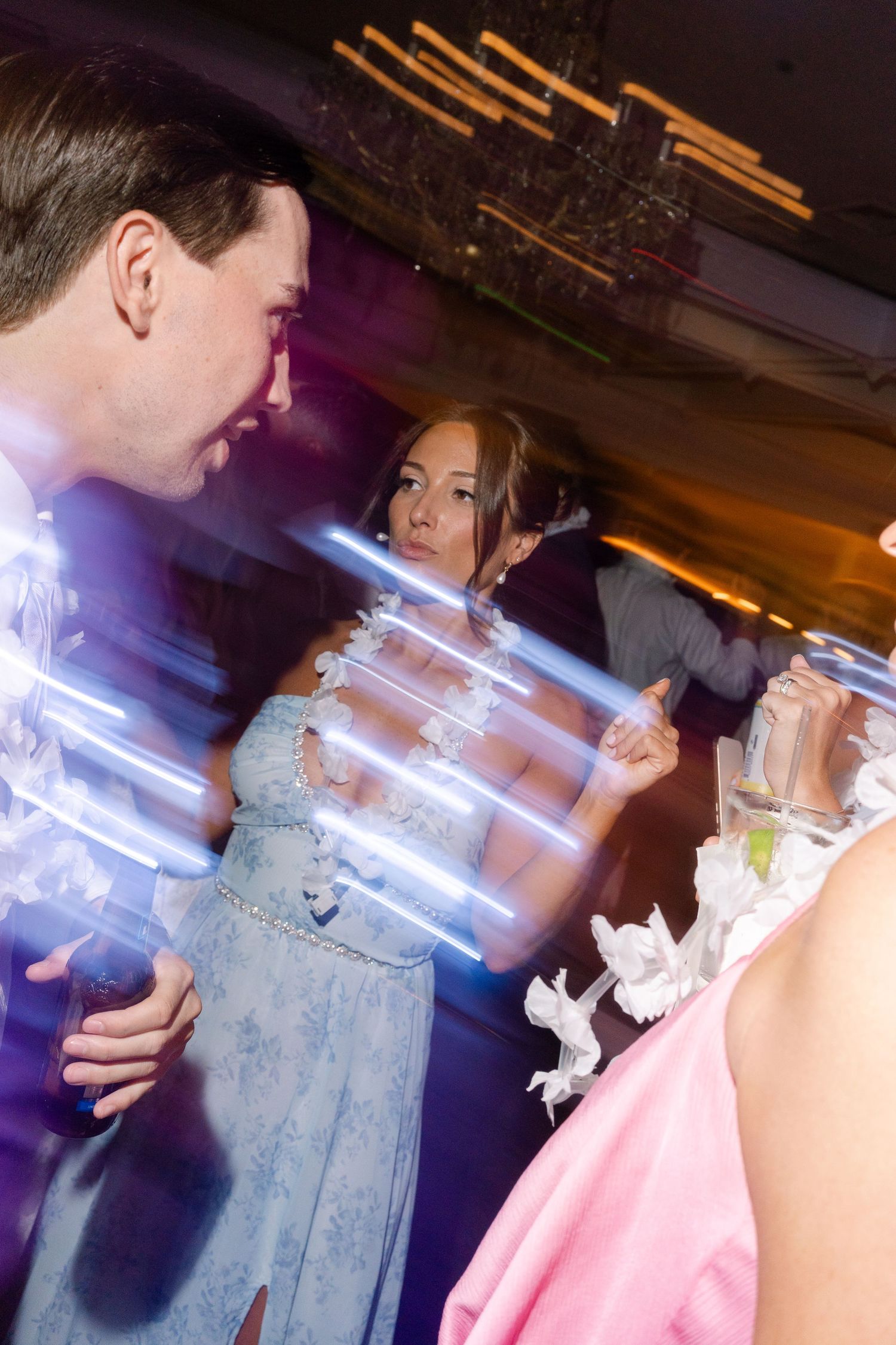 People dancing at a formal event with light streaks, woman in blue gown visible under colorful party lights.