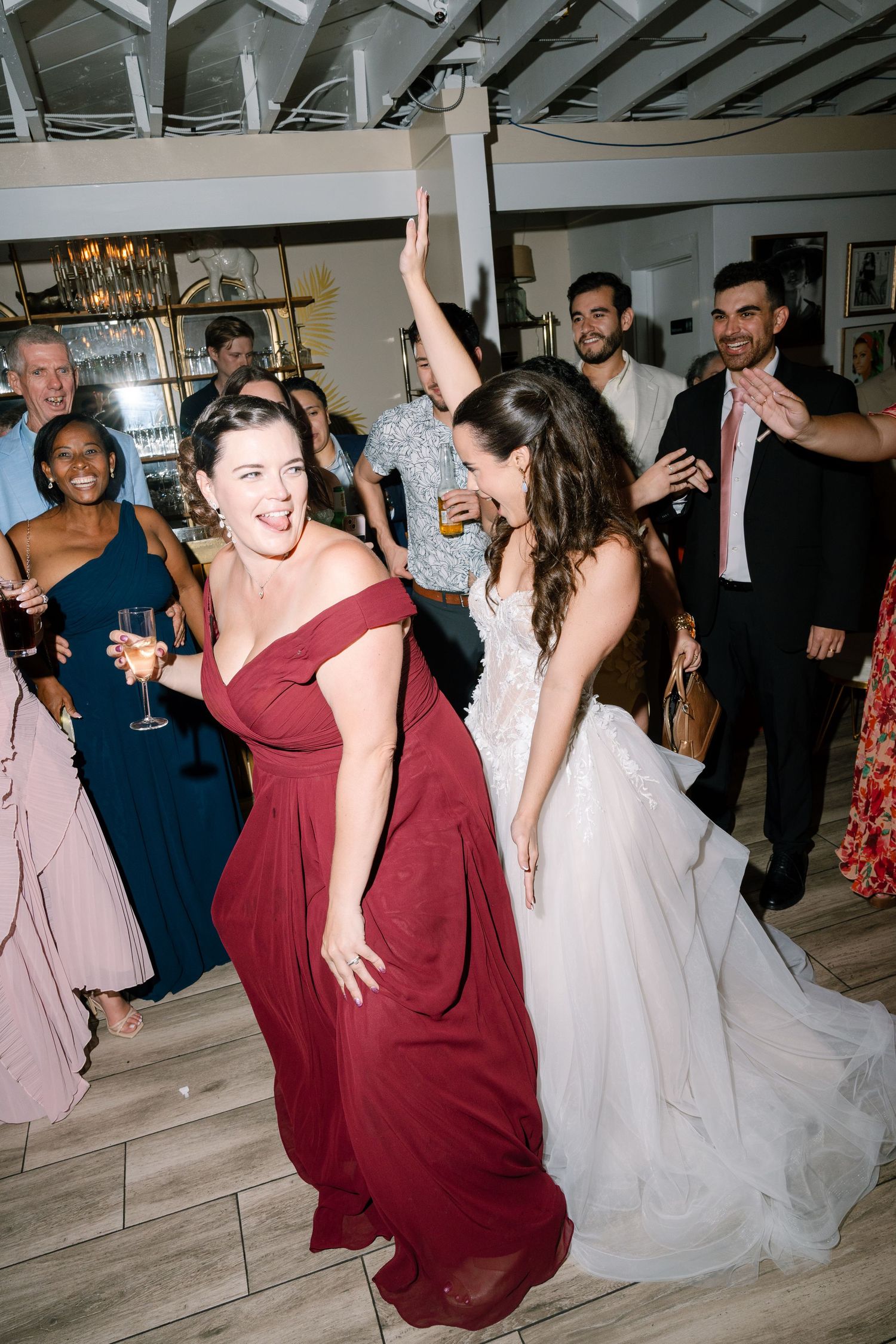 Bride in white gown dances energetically with bridesmaid in red dress at wedding reception.
