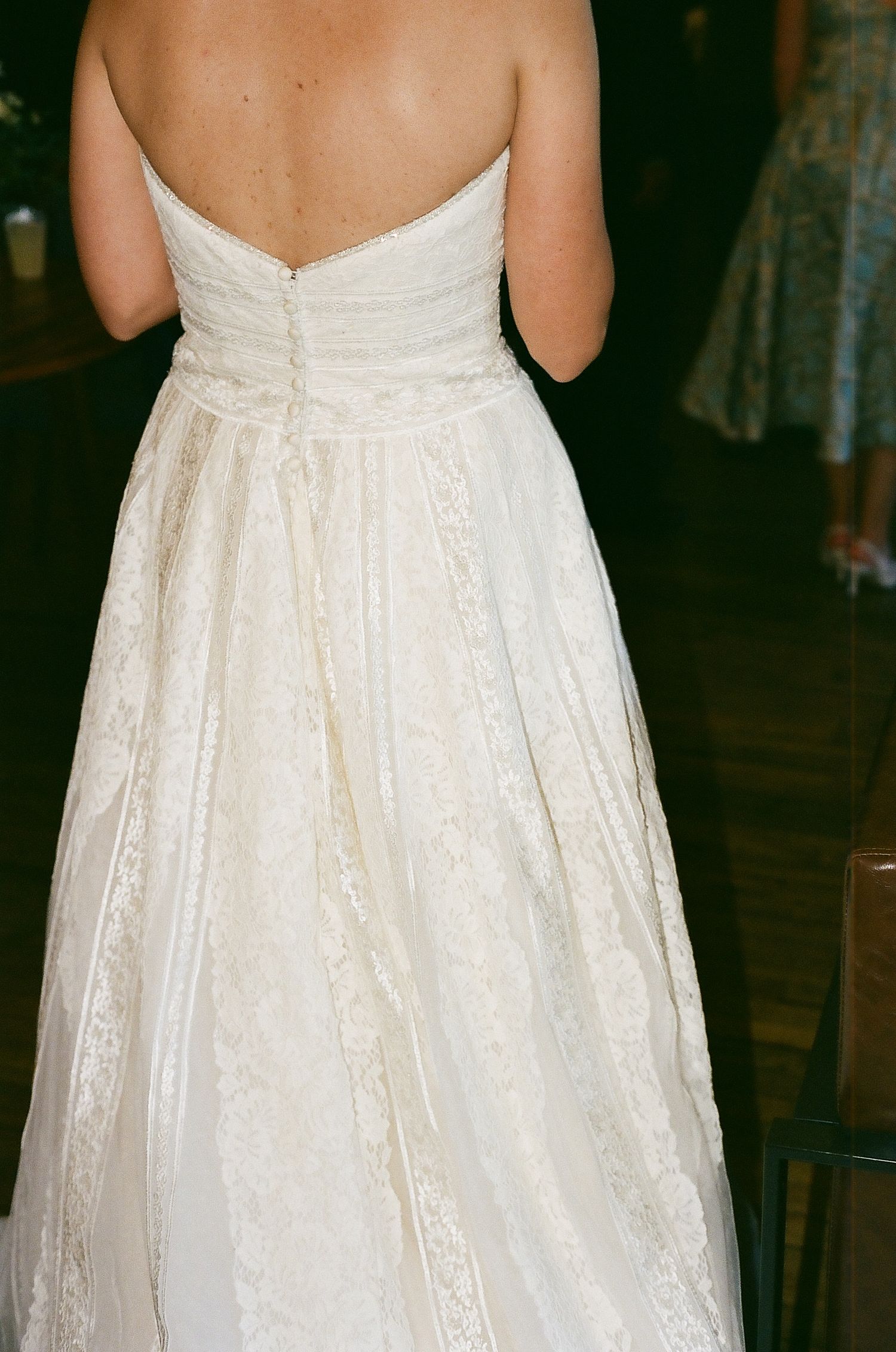 Back detail of a strapless white wedding gown with intricate lace and button closures.